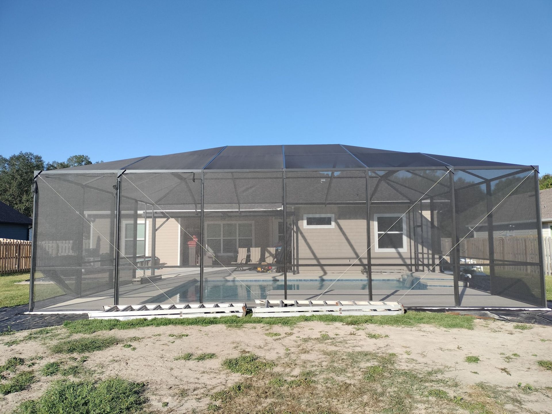 A screened in swimming pool with a house in the background