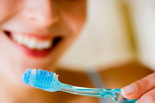 A Woman Is Brushing Her Teeth with A Blue Toothbrush