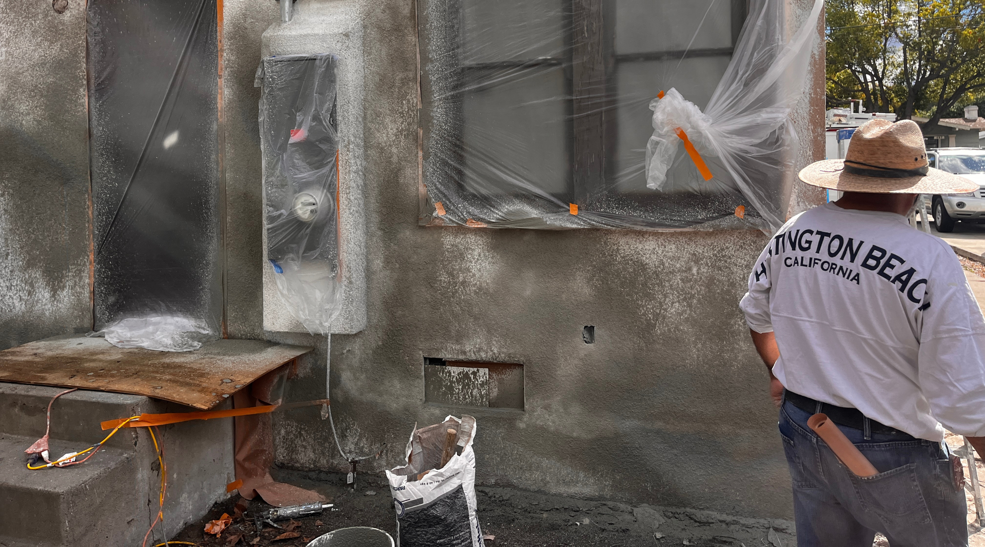 A bathroom undergoing renovation with unfinished drywall, exposed plumbing pipes, and a toilet on a plastic-covered floor.