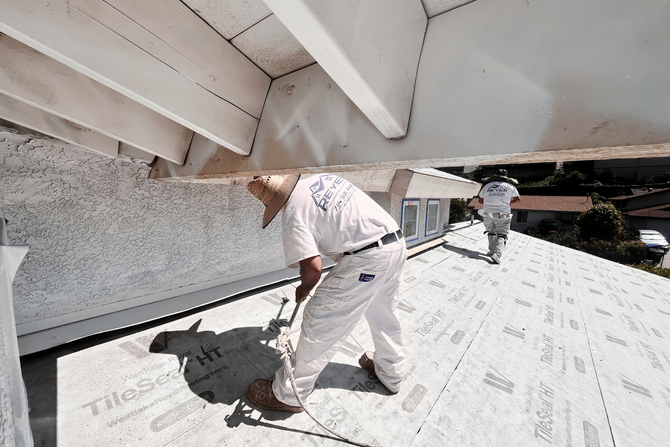 A white pickup truck with a ladder rack and a white work van parked side-by-side in front of a beige building wall.