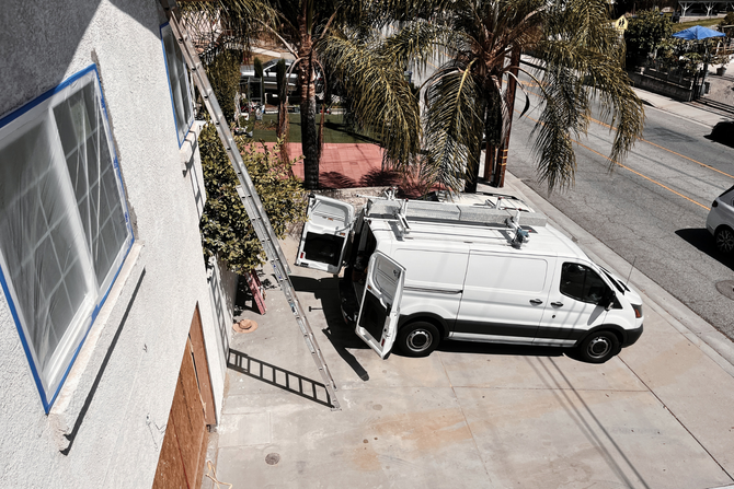 Workers renovate an oceanfront room with floor-to-ceiling glass doors, ladders, and building materials.