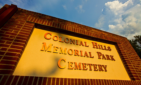 Sign for Colonial Hills Memorial Park Cemetery in brick, tan, and orange against a blue sky.
