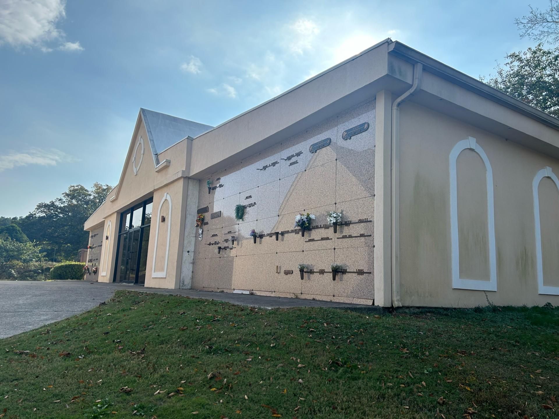 Cemetery mausoleum building with dark doors and grave markers on a sunny day.