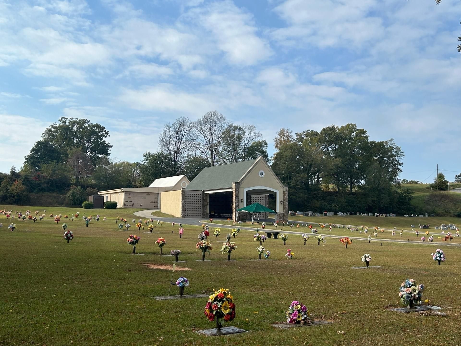 Cemetery with green grass, headstones, and a small chapel building under a blue sky with clouds.