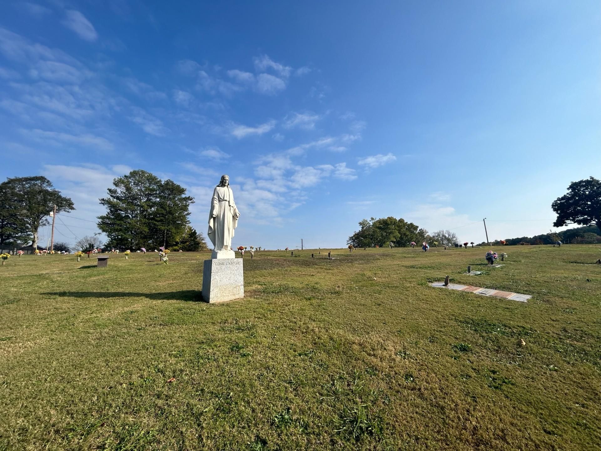 White statue of a woman in a cemetery on a grassy hill under a blue sky.
