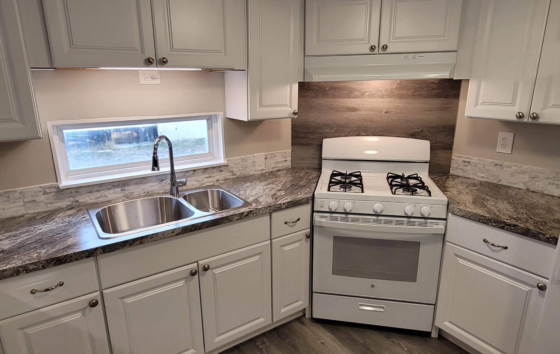 A kitchen with white cabinets , granite counter tops , a stove and a sink.