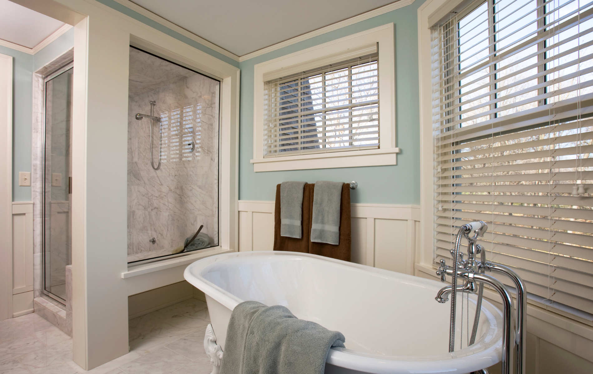 A bathroom with a tub , shower and window with blinds.