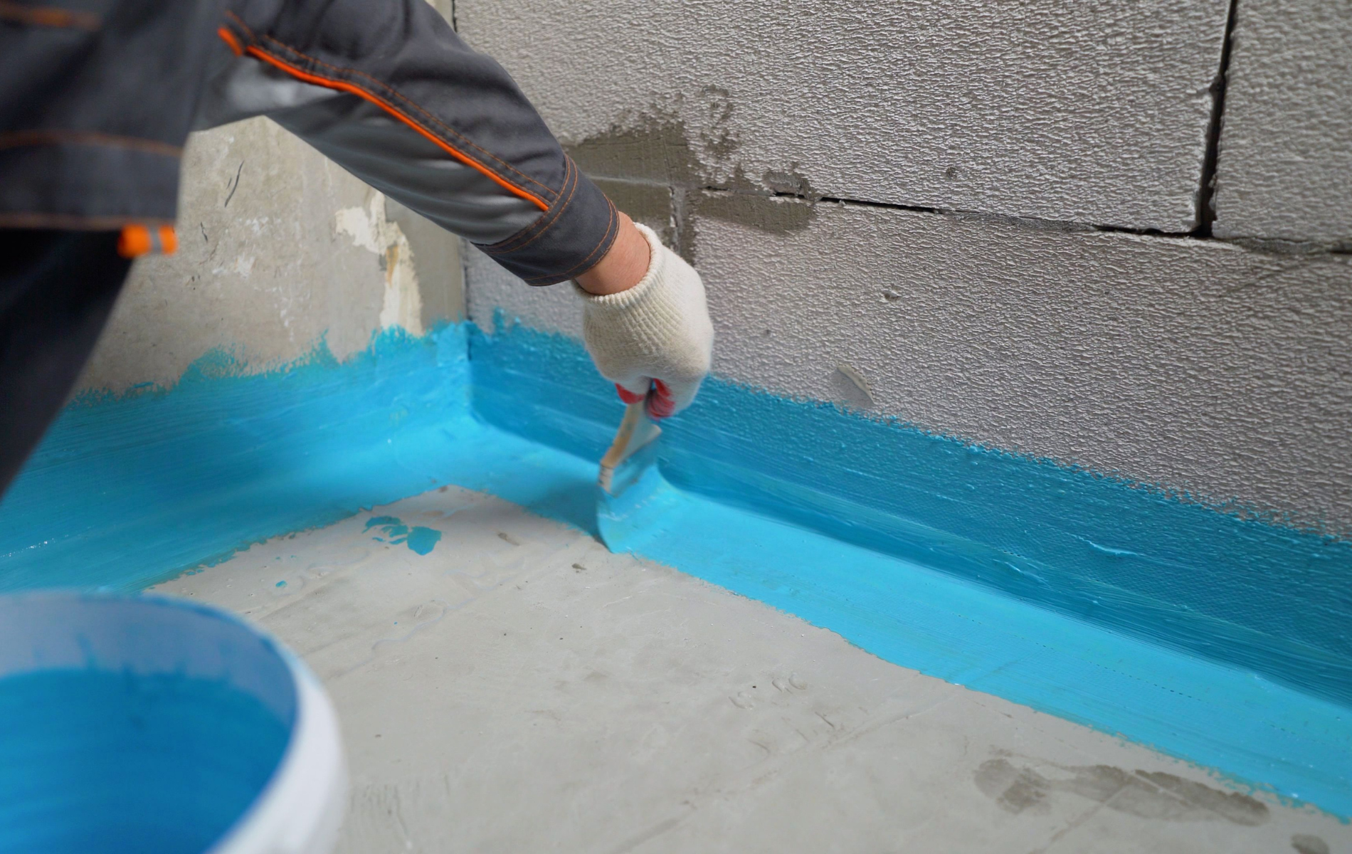 A person is painting a corner of a bathroom floor with blue paint.