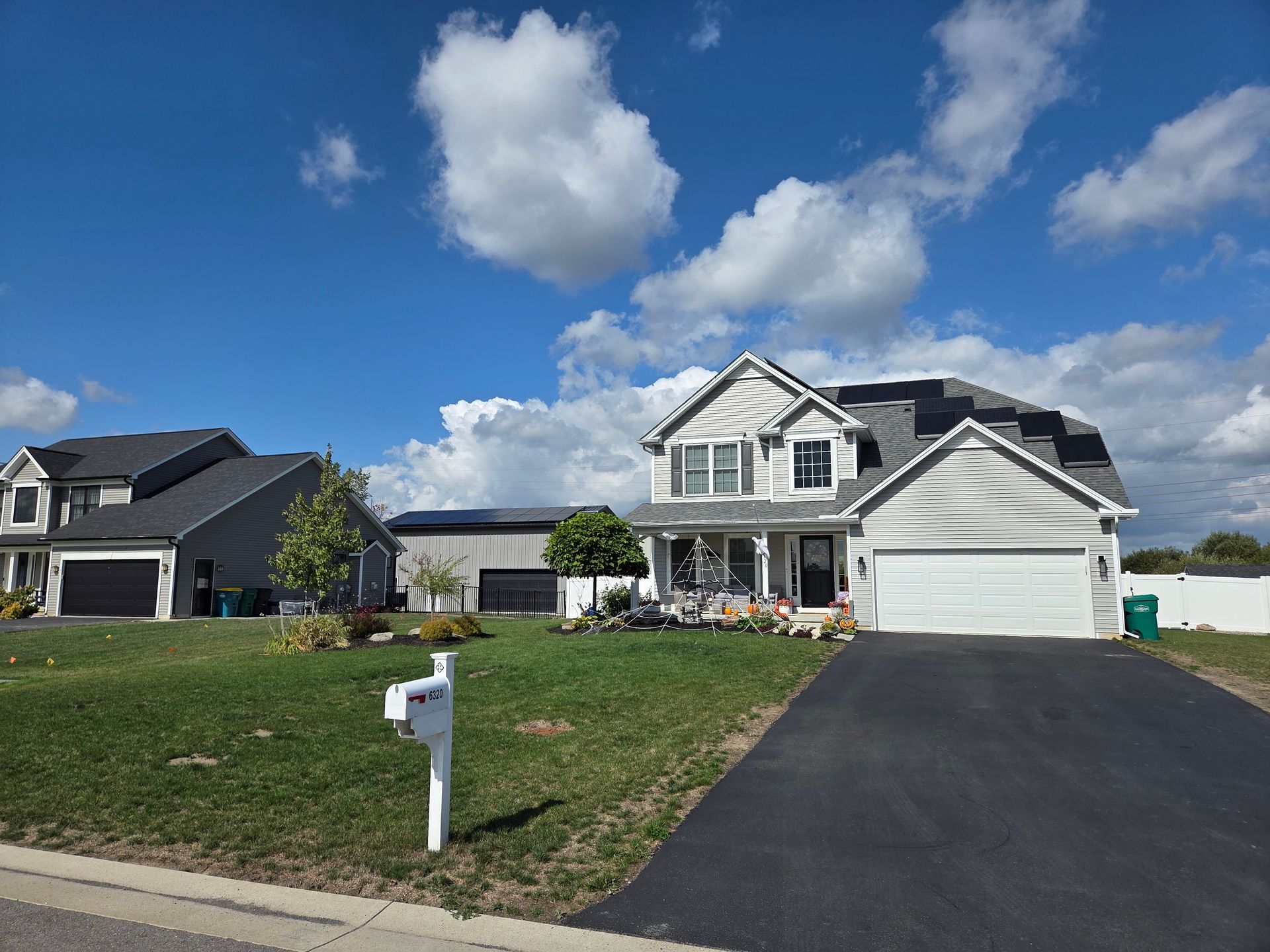 Houses on a sunny day with blue sky, white clouds, and green grass. A mailbox and driveway are in the foreground.