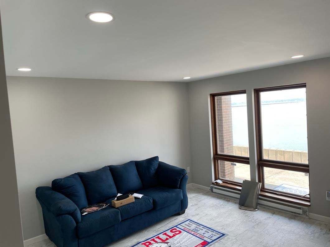 A living room with a blue couch and two windows.
