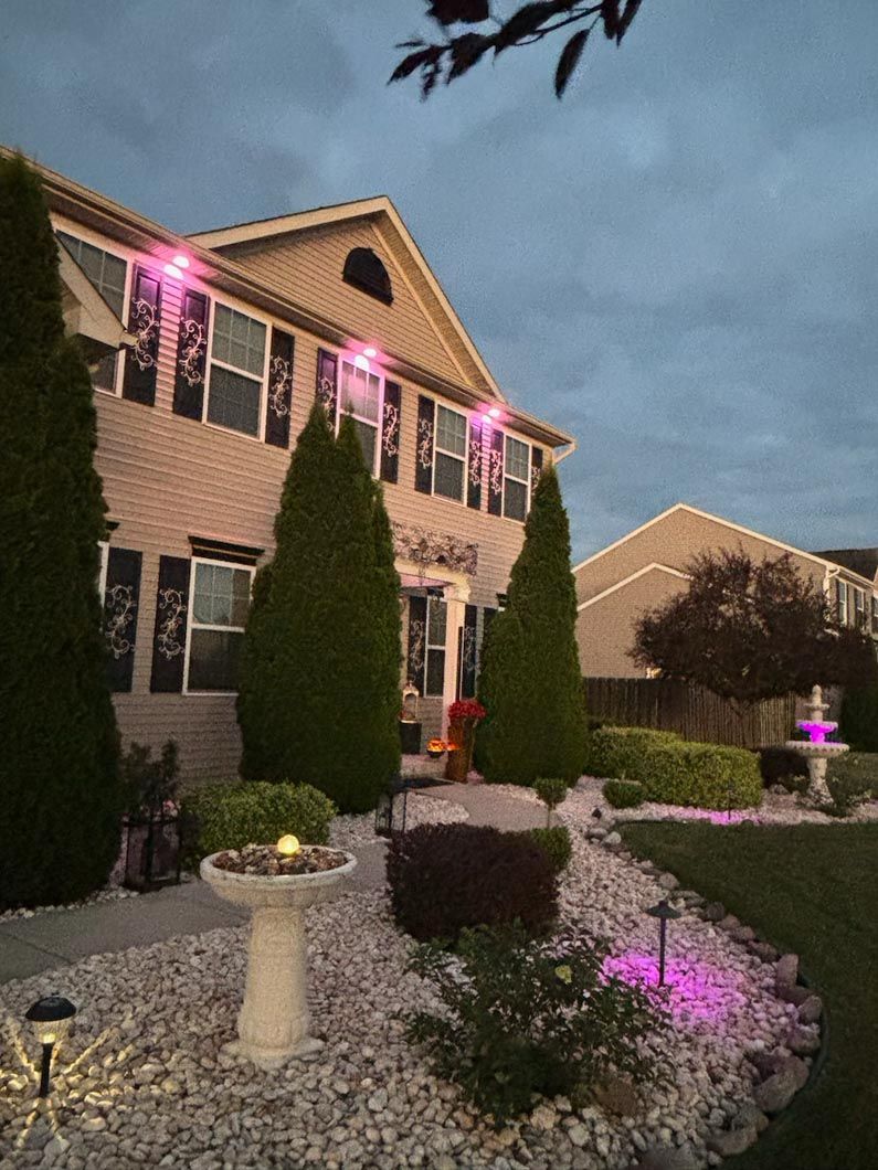 A house with pink lights on the windows and a fountain in front of it.