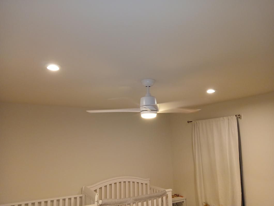 A bedroom with two cribs and a ceiling fan