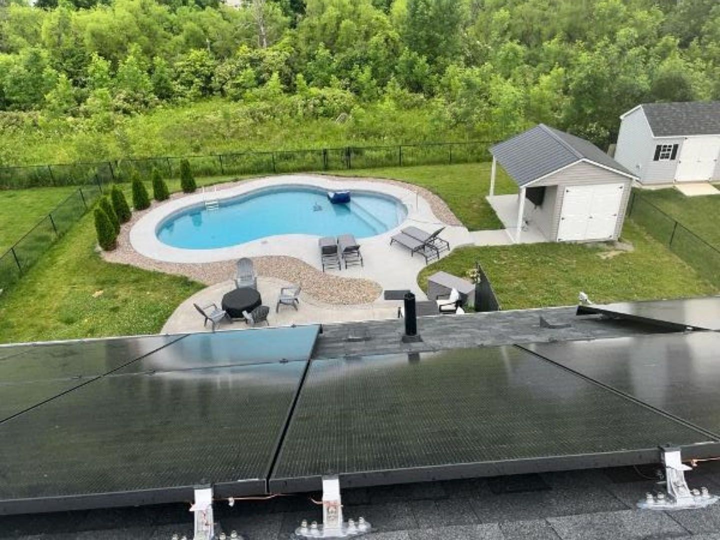 A view of a swimming pool from the roof of a house with a solar panel on the roof.