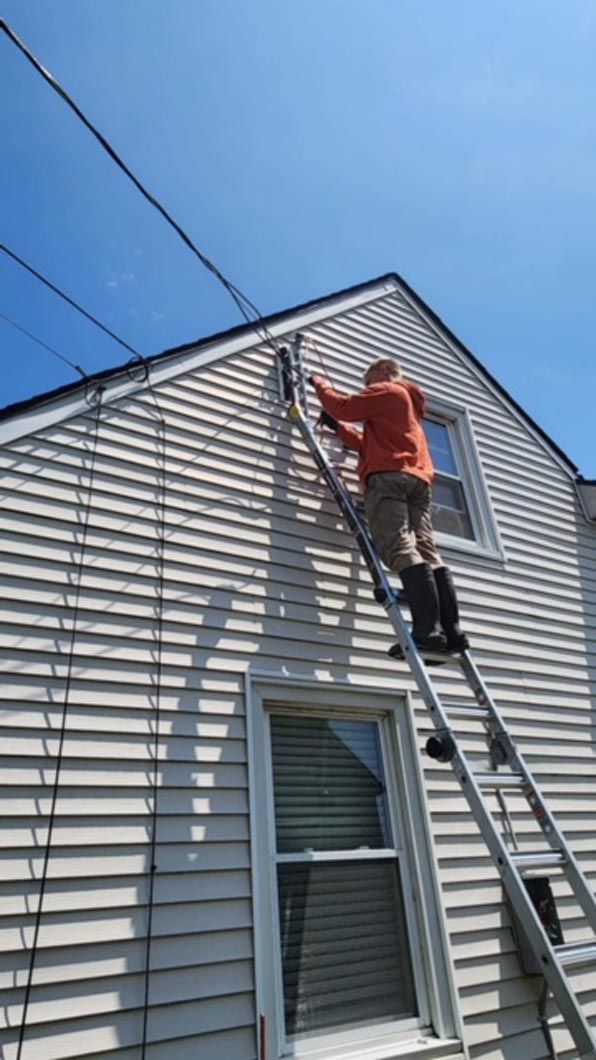A man is standing on a ladder on the side of a house.