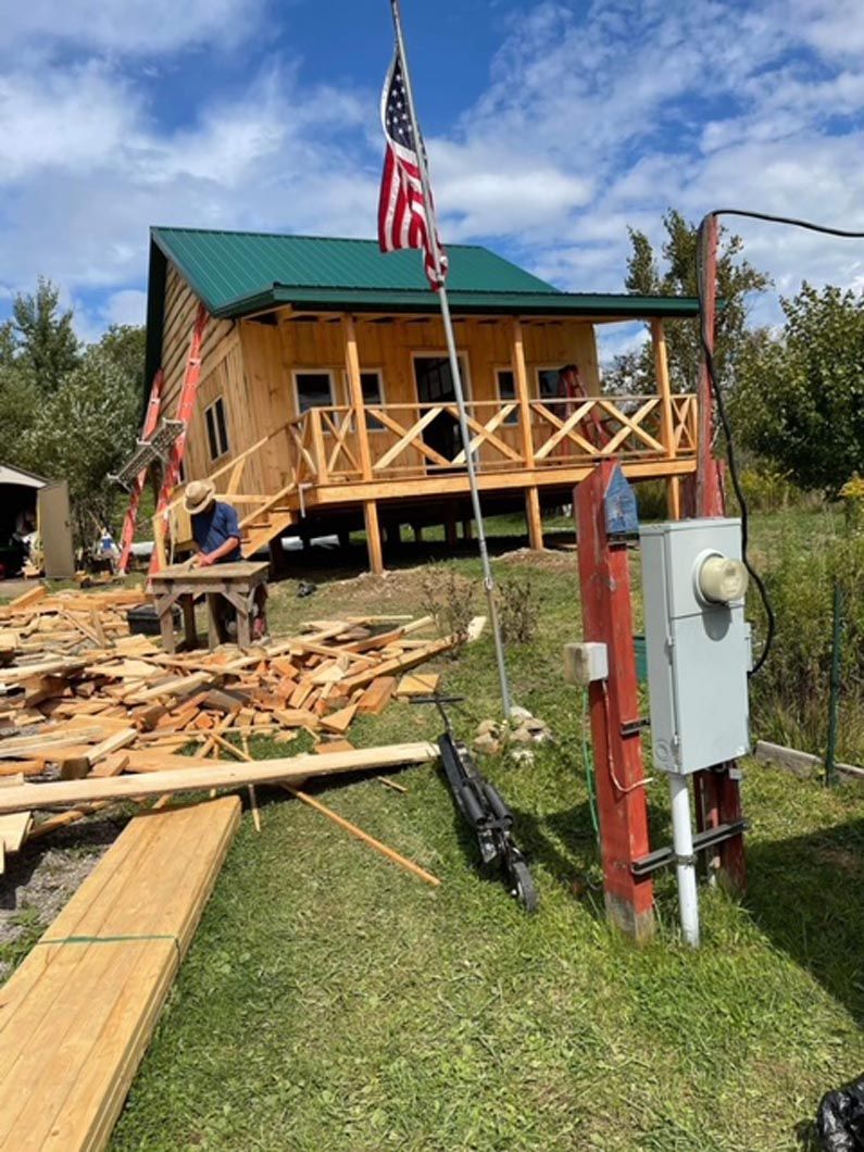 A wooden house with a green roof and a porch is being built.