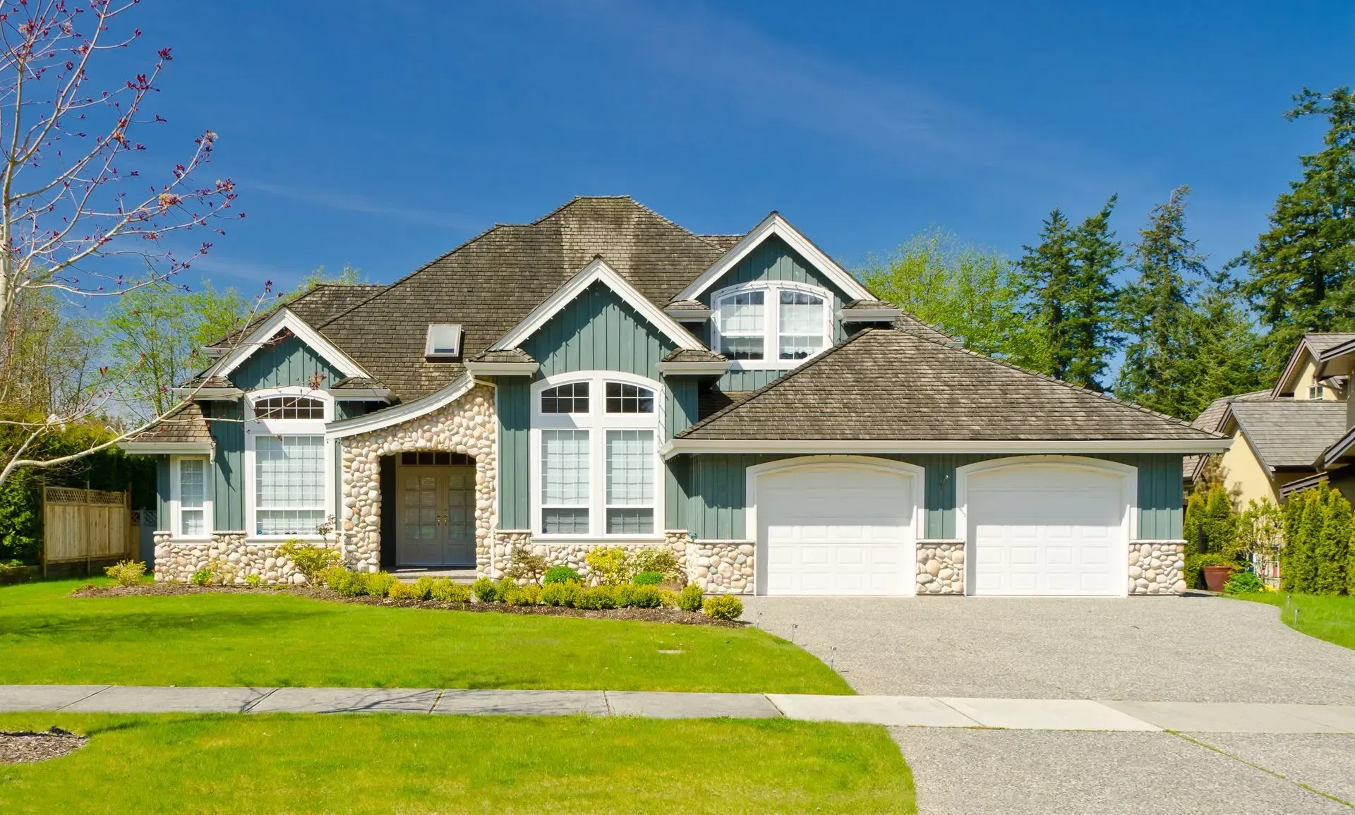 Suburban house with gray siding, white trim, stone accents, and a two-car garage on a sunny day