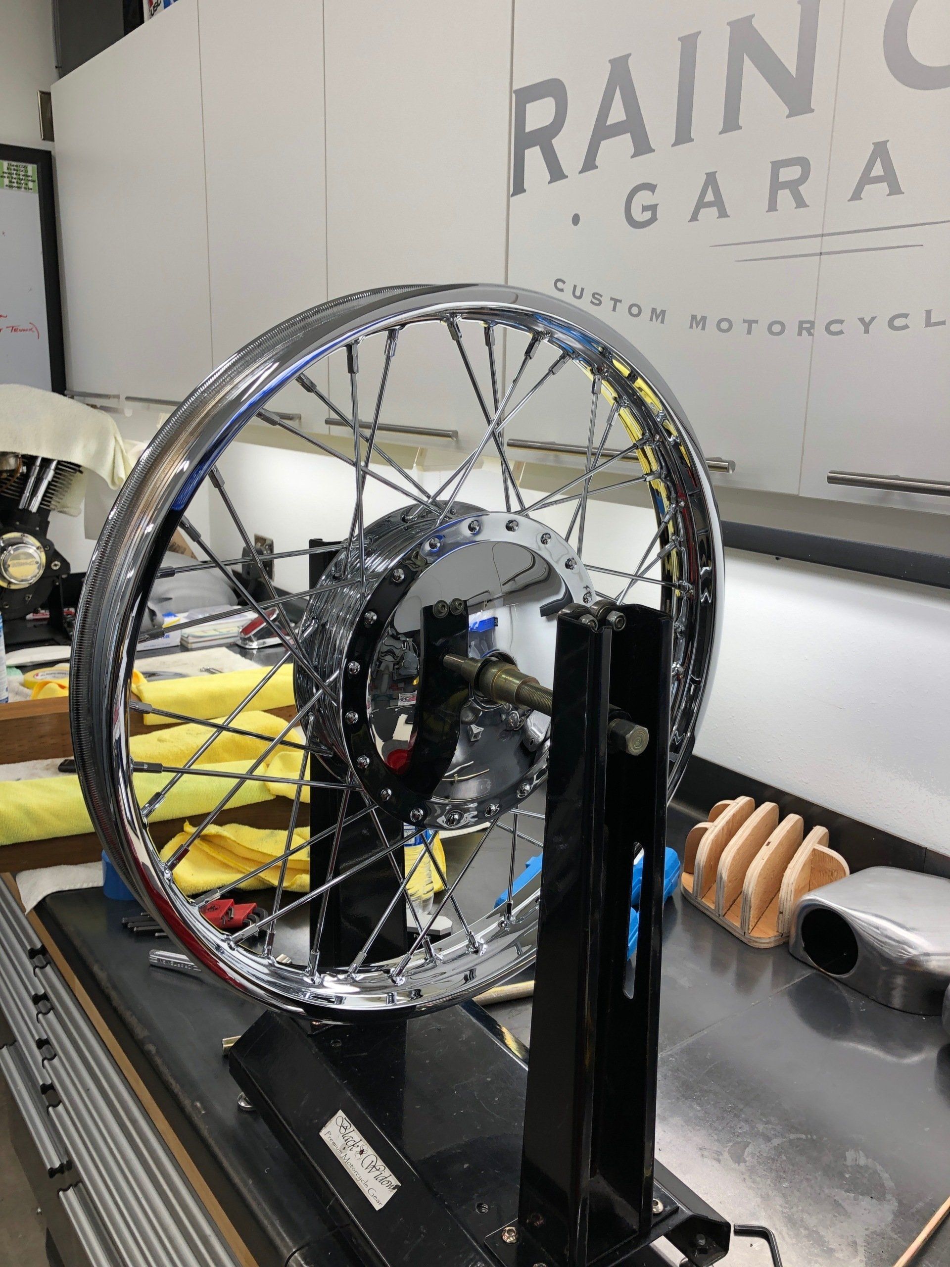 A motorcycle wheel is being worked on in front of a sign that says rain garage