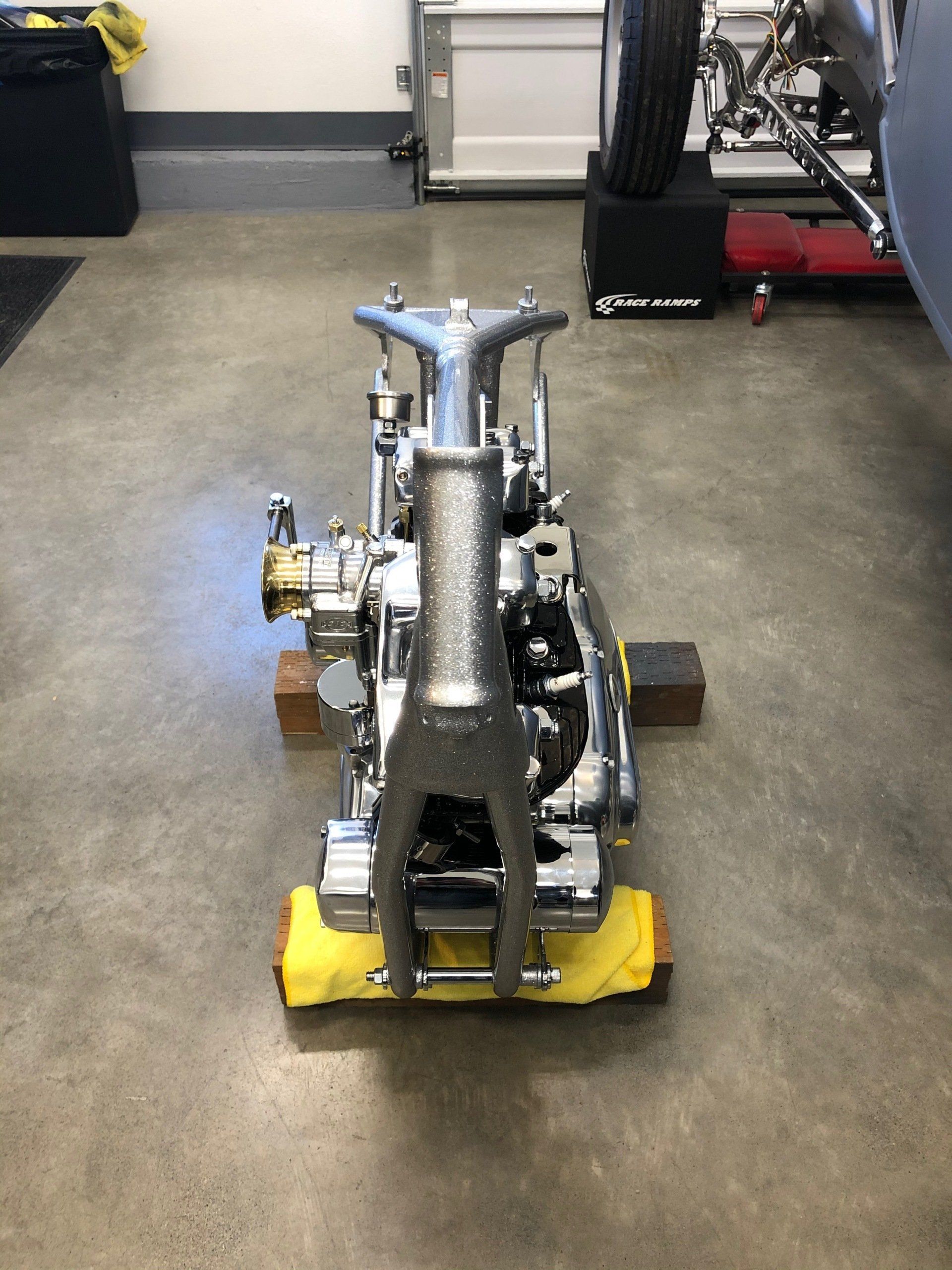 A motorcycle frame is sitting on a yellow cloth in a garage.