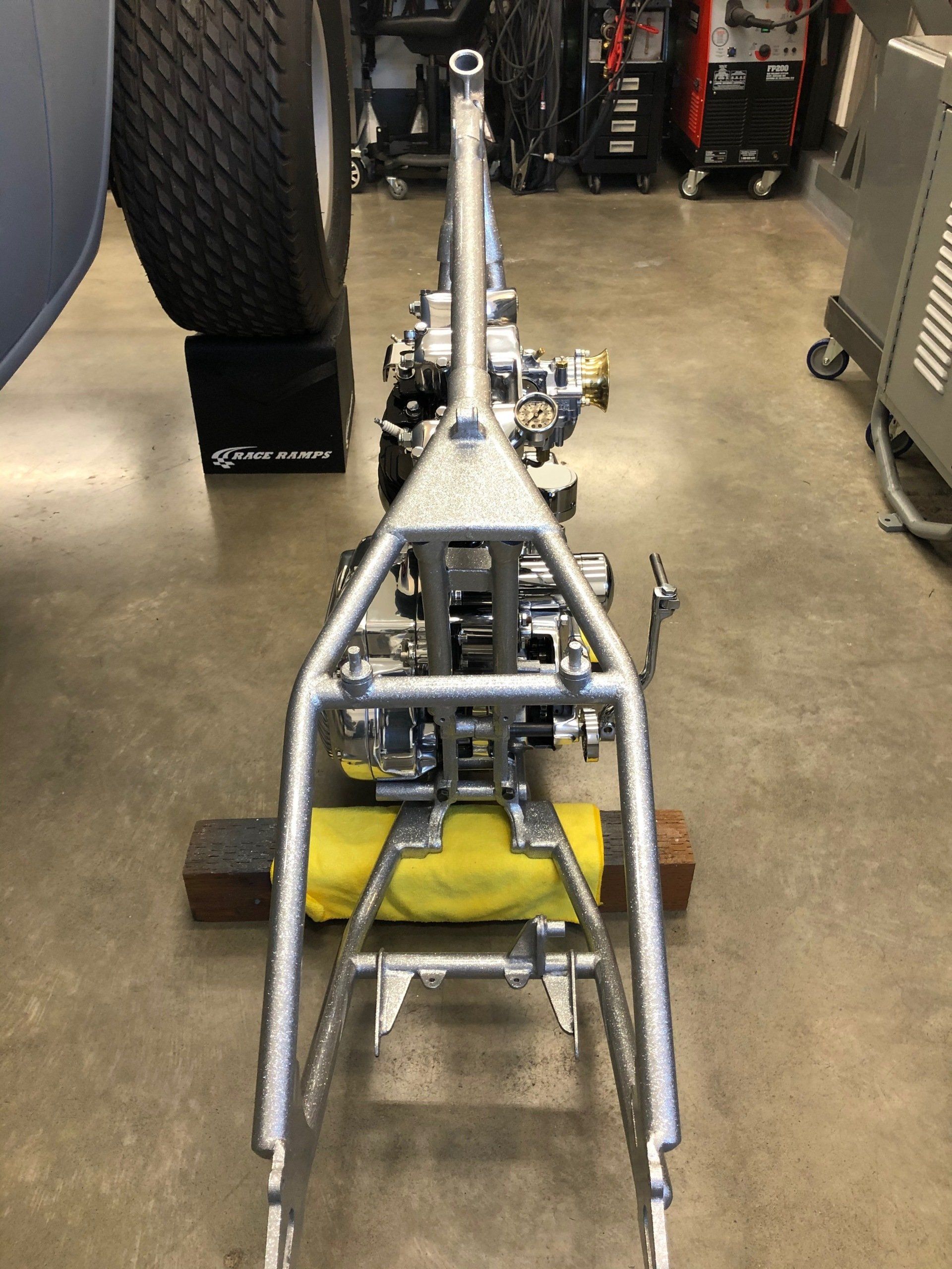 A motorcycle frame is sitting on a wooden block in a garage.