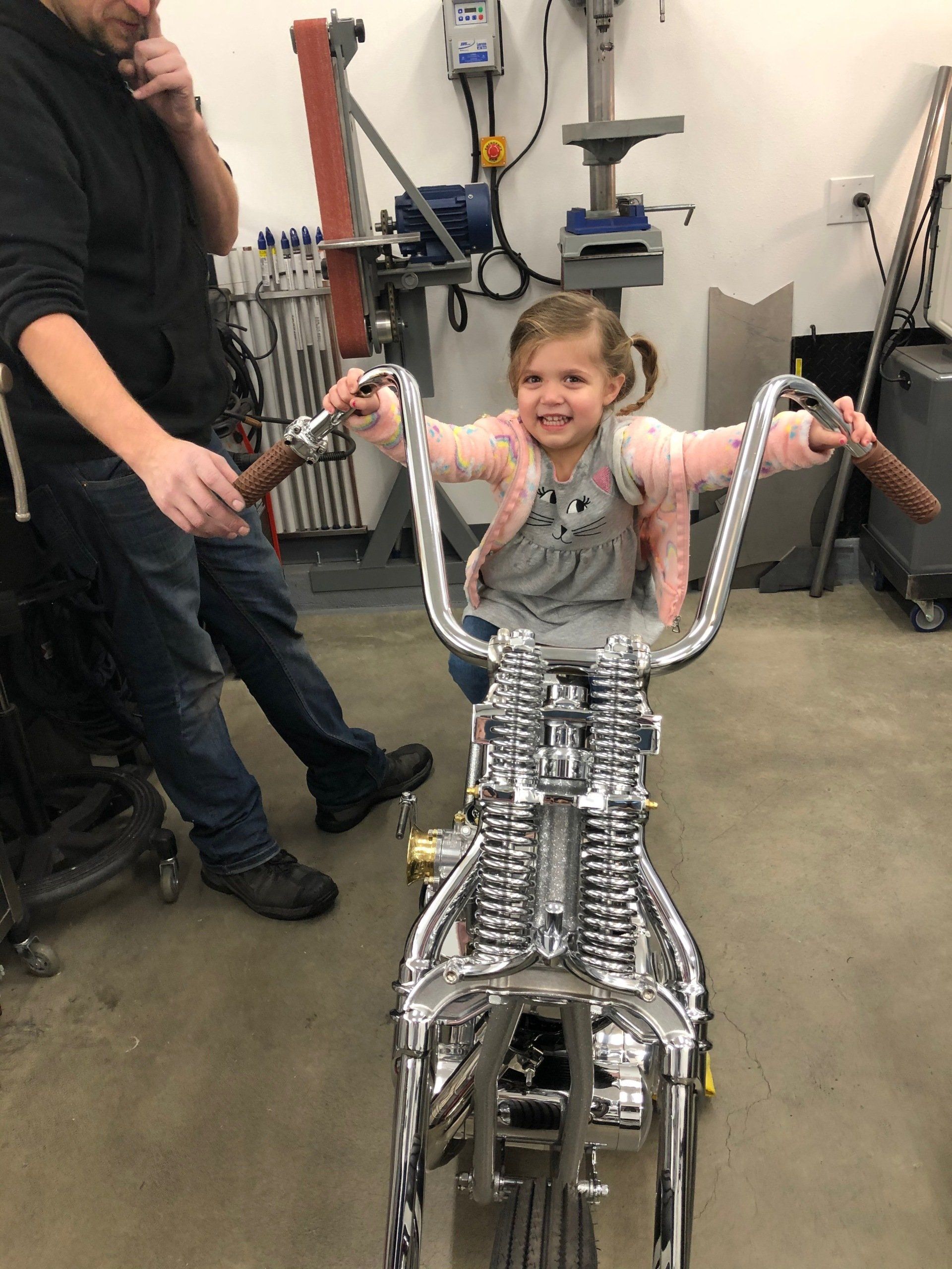 A little girl is sitting on a motorcycle with a man standing behind her