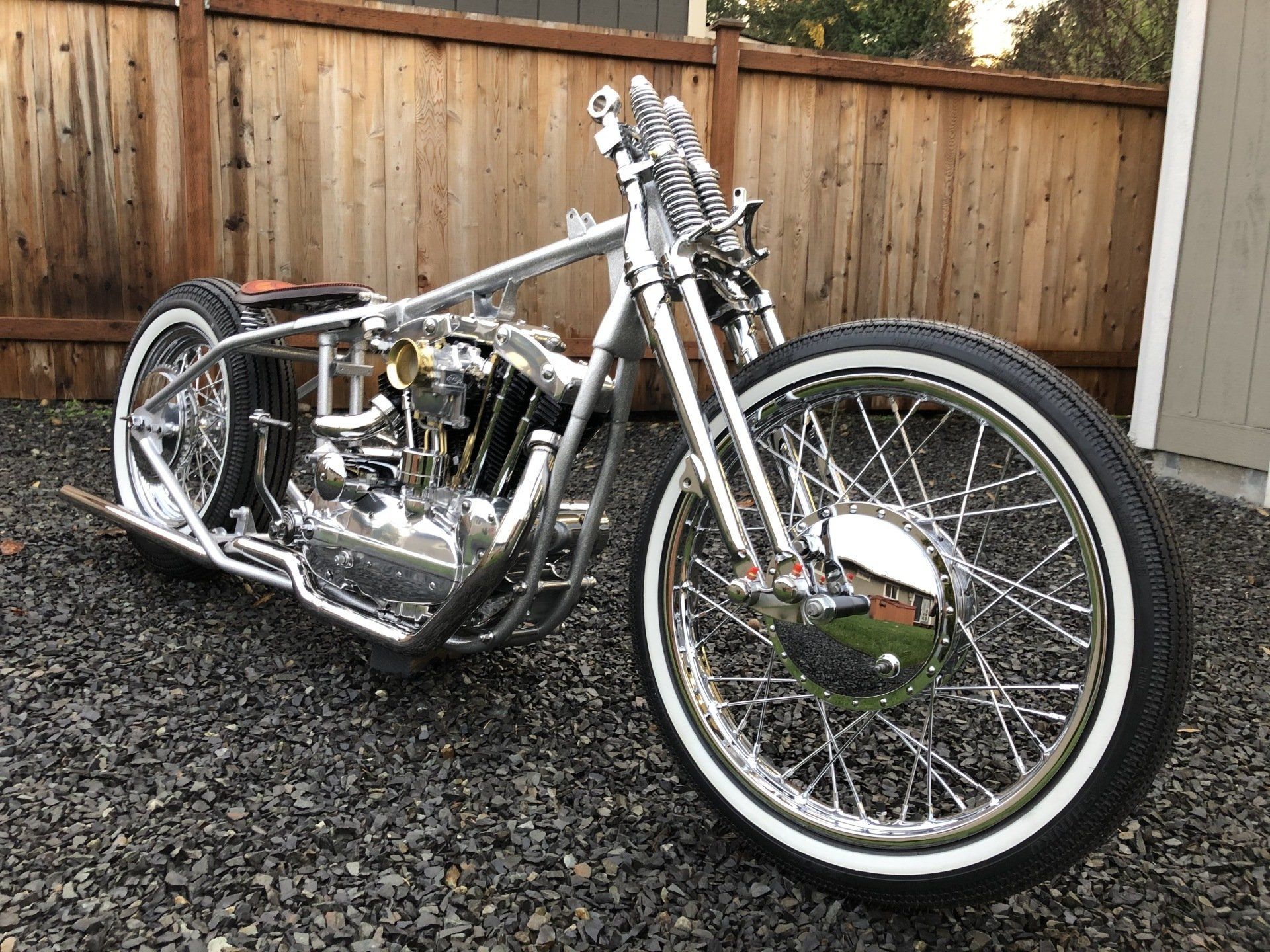 A motorcycle is parked on gravel in front of a wooden fence.