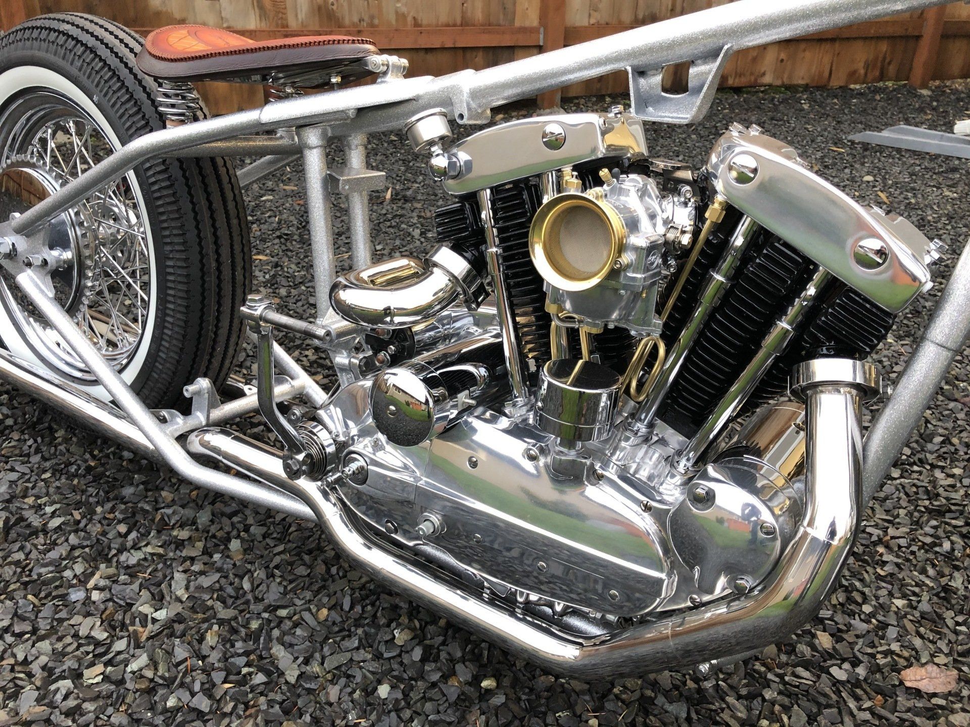 A motorcycle is parked on gravel in front of a wooden fence.