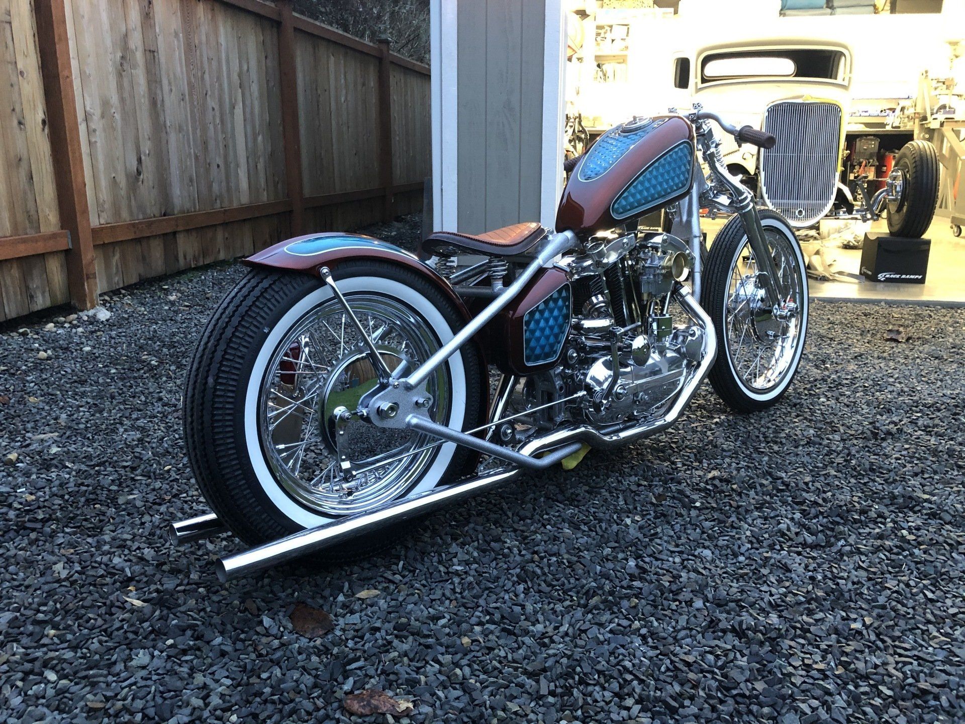 A motorcycle is parked in a gravel lot next to a wooden fence.