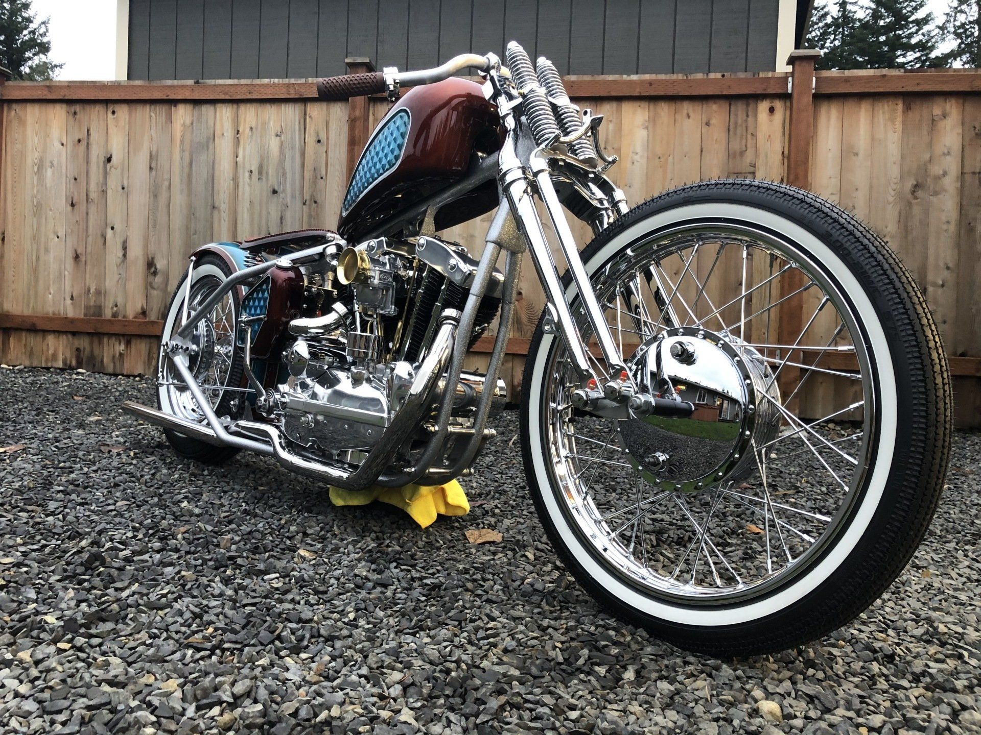 A motorcycle is parked on gravel in front of a wooden fence.