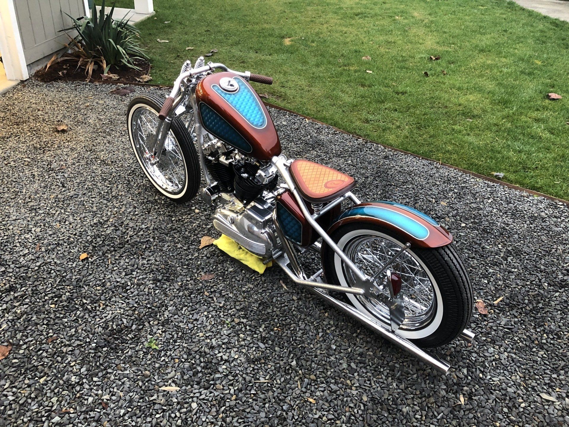 A chopper motorcycle is parked on gravel in a driveway.