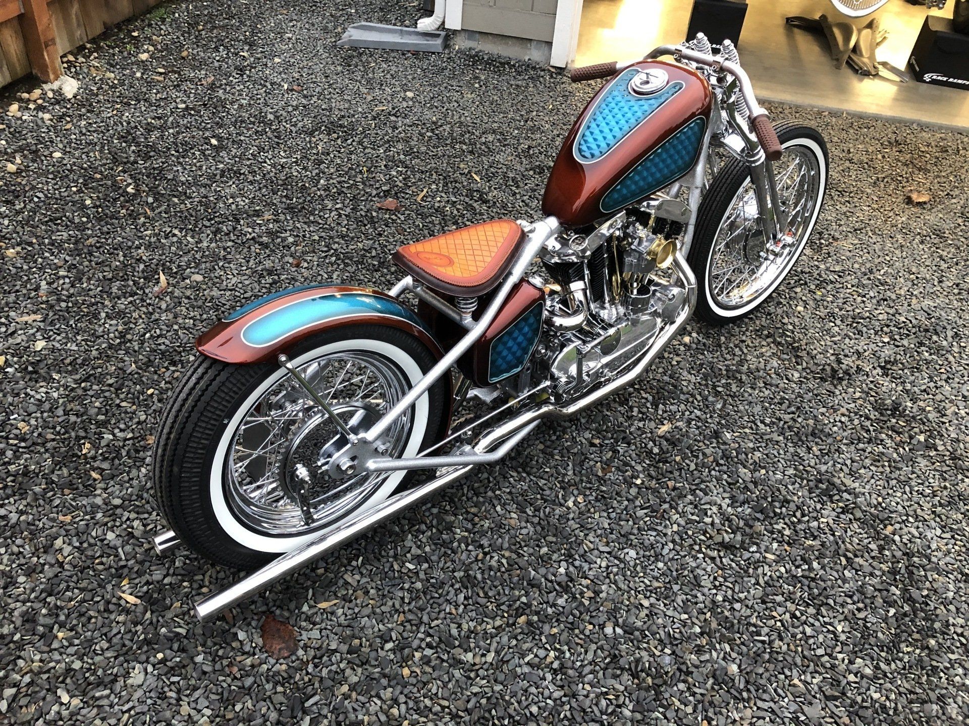 A chopper motorcycle is parked in a gravel lot.