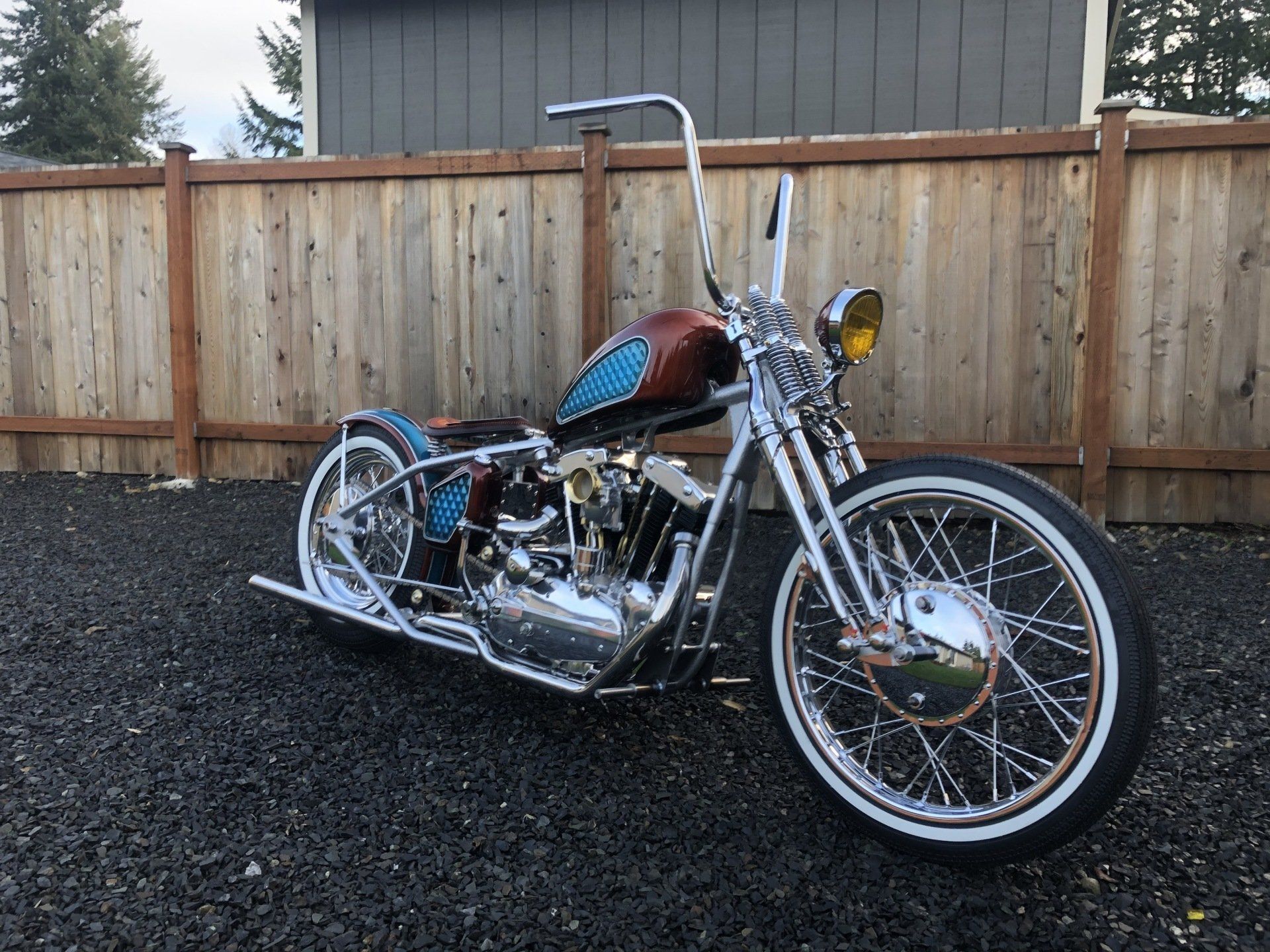A chopper motorcycle is parked in front of a wooden fence.