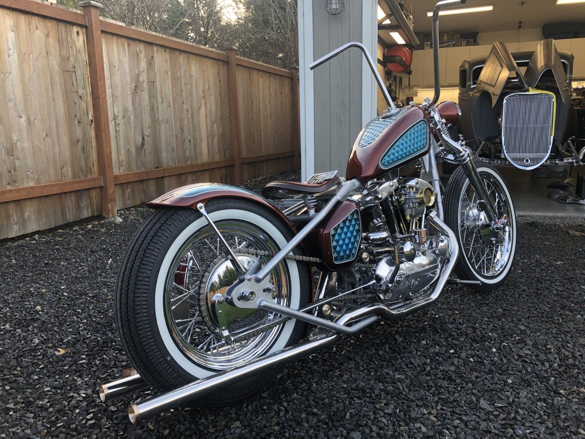 A motorcycle is parked in a gravel lot next to a wooden fence.