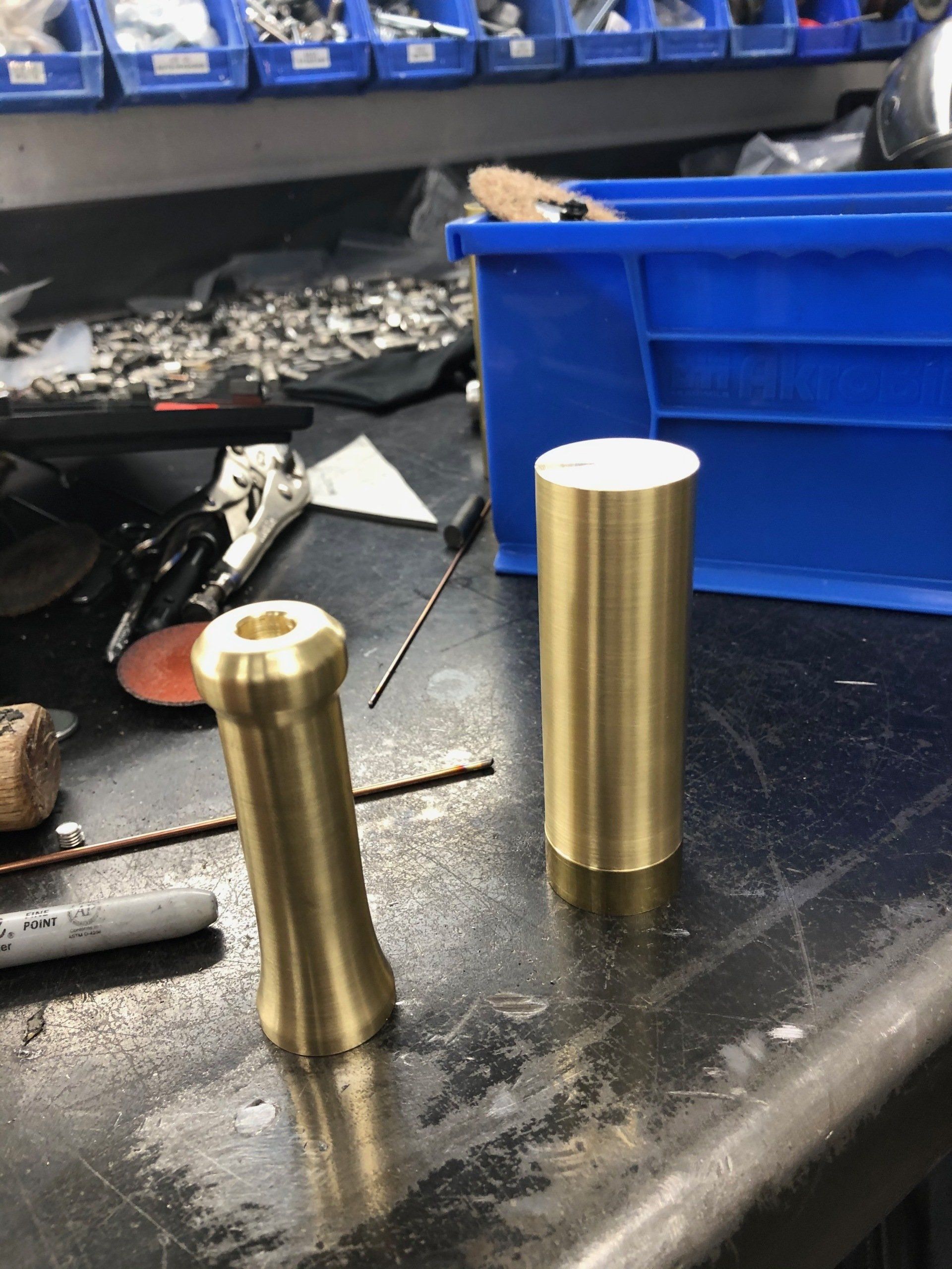Two brass cylinders are sitting on a table next to a blue bin
