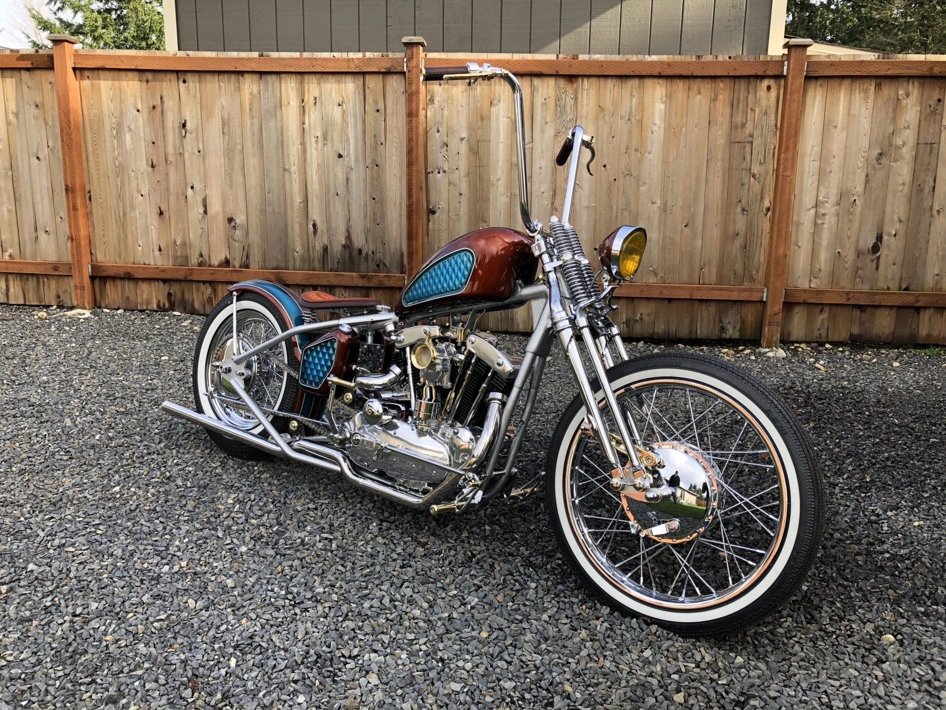 A chopper motorcycle is parked in front of a wooden fence.