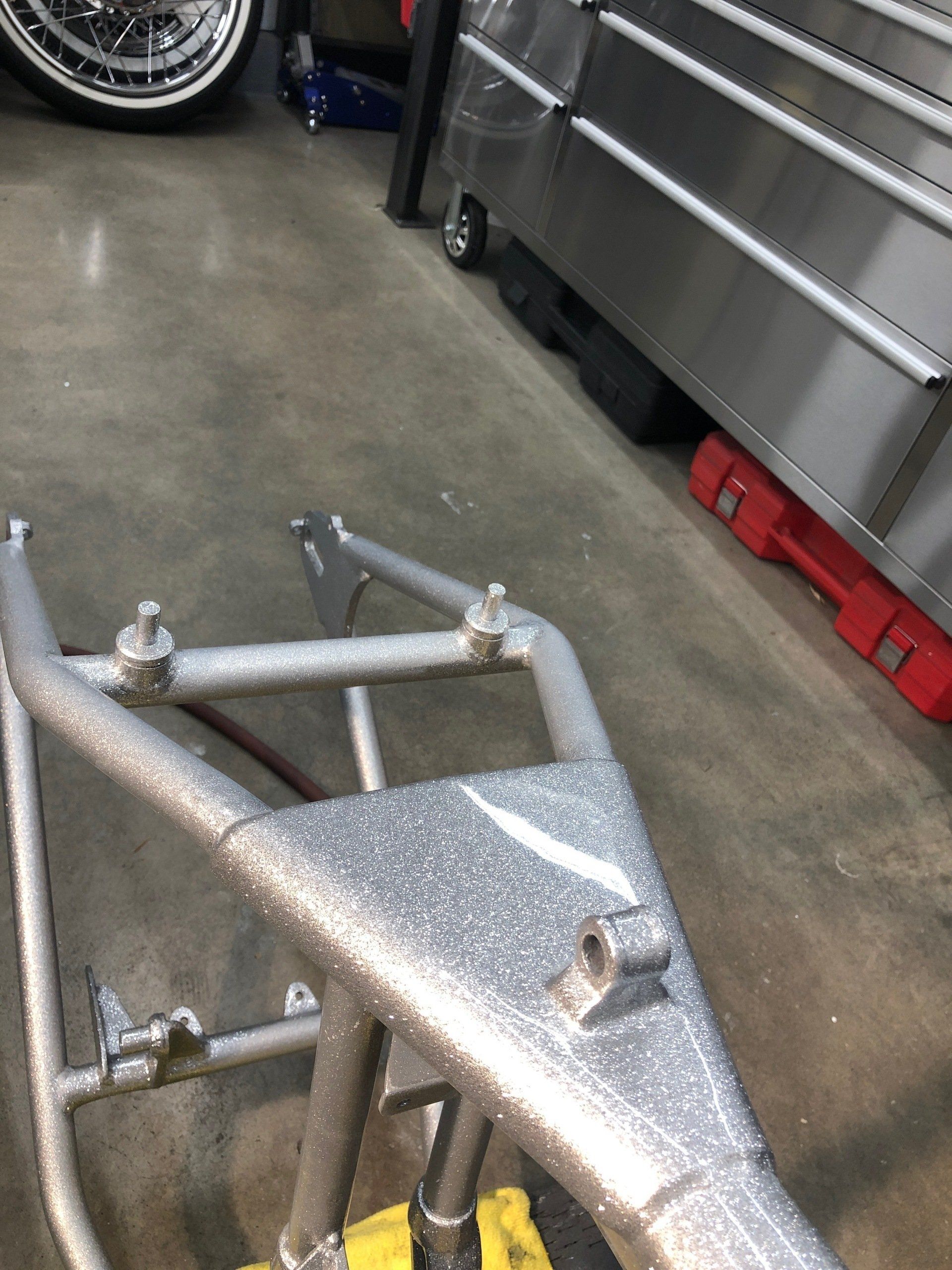 A motorcycle frame is sitting on a concrete floor in a garage.