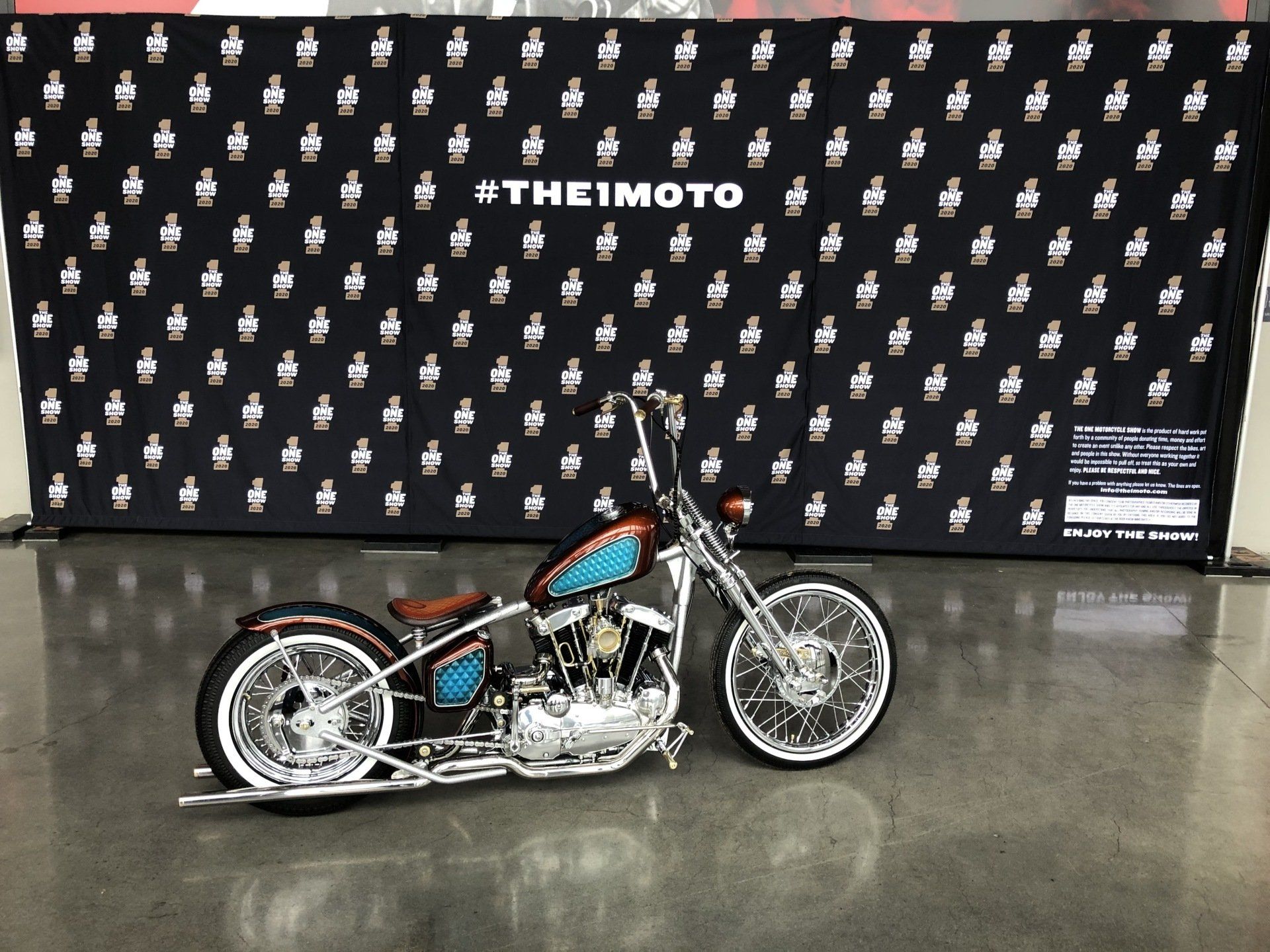 A motorcycle is parked in front of a wall that says theimoto