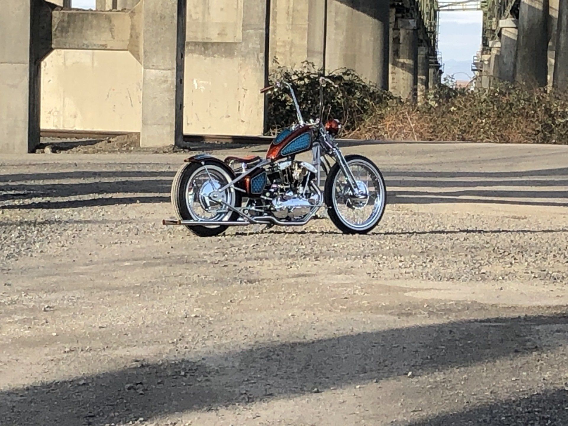 A motorcycle is parked in a gravel lot under a bridge.