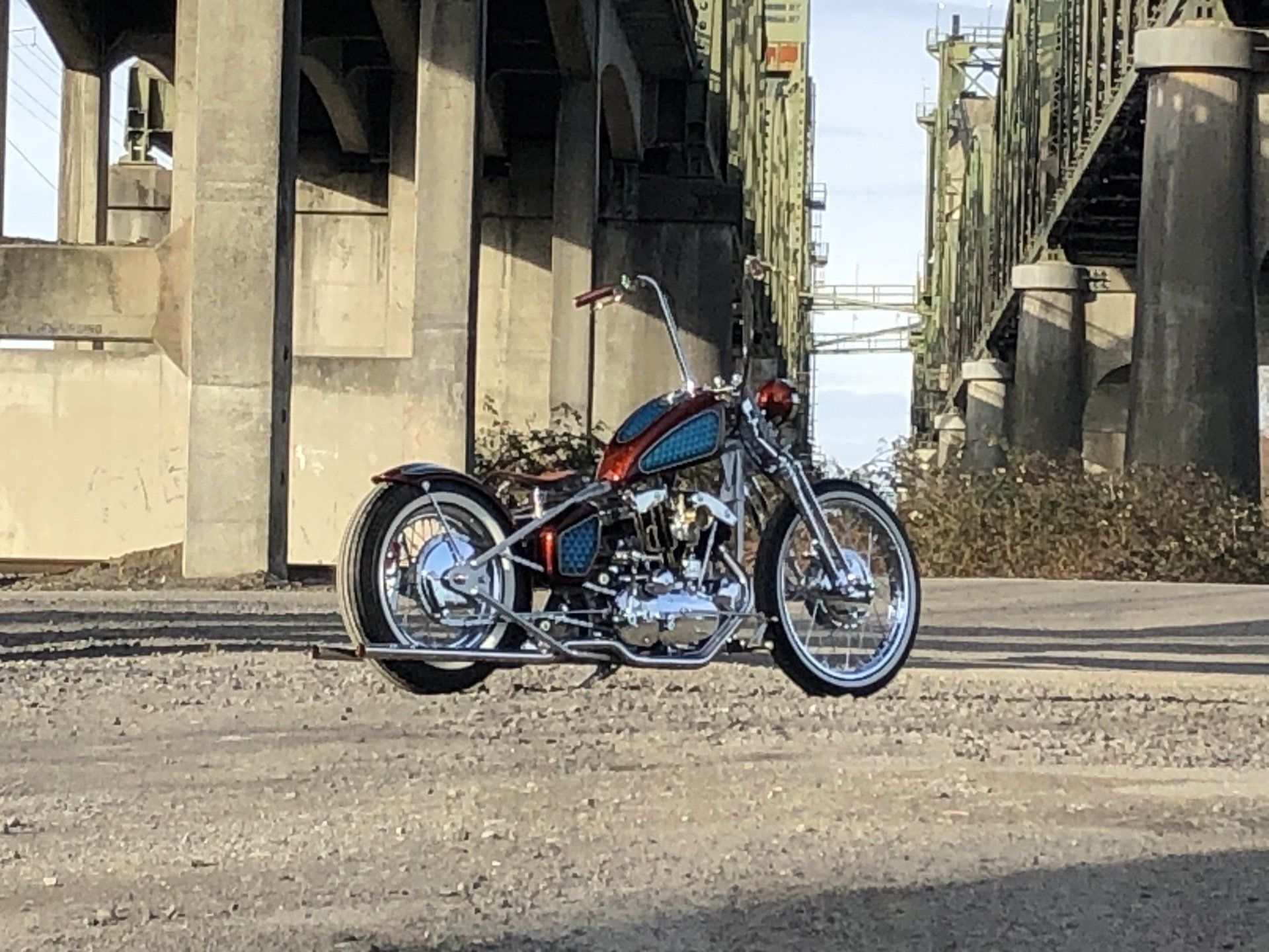 A motorcycle is parked on the side of the road under a bridge.