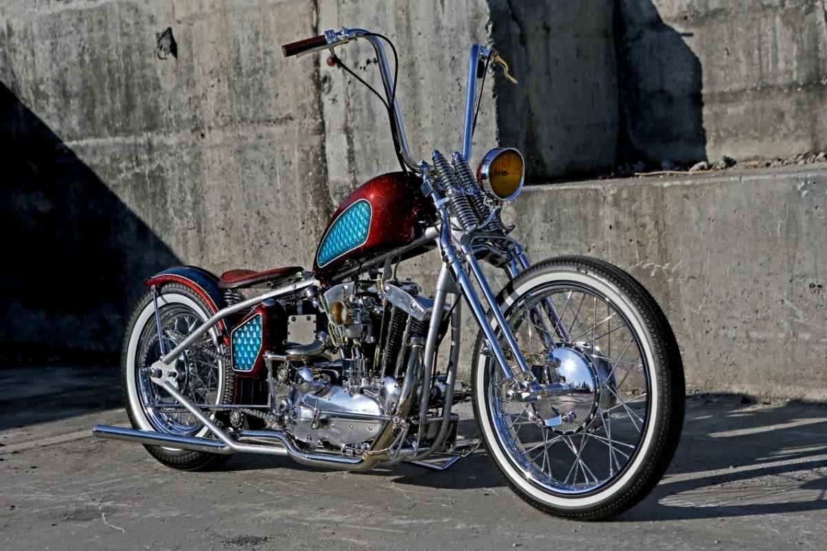A chopper motorcycle is parked in front of a concrete wall.