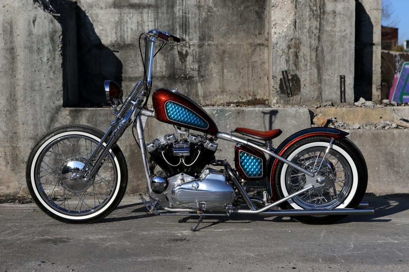 A chopper motorcycle is parked in front of a concrete wall.