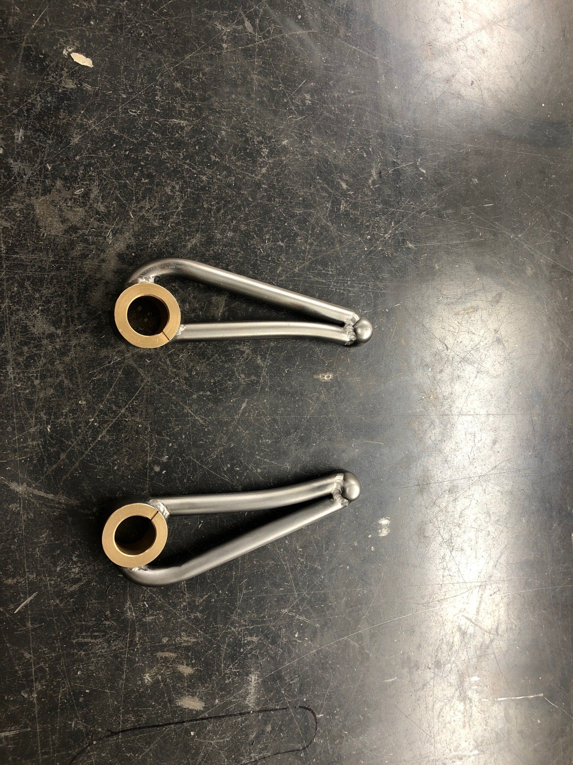 Two metal pieces with holes in them are sitting on a black surface.