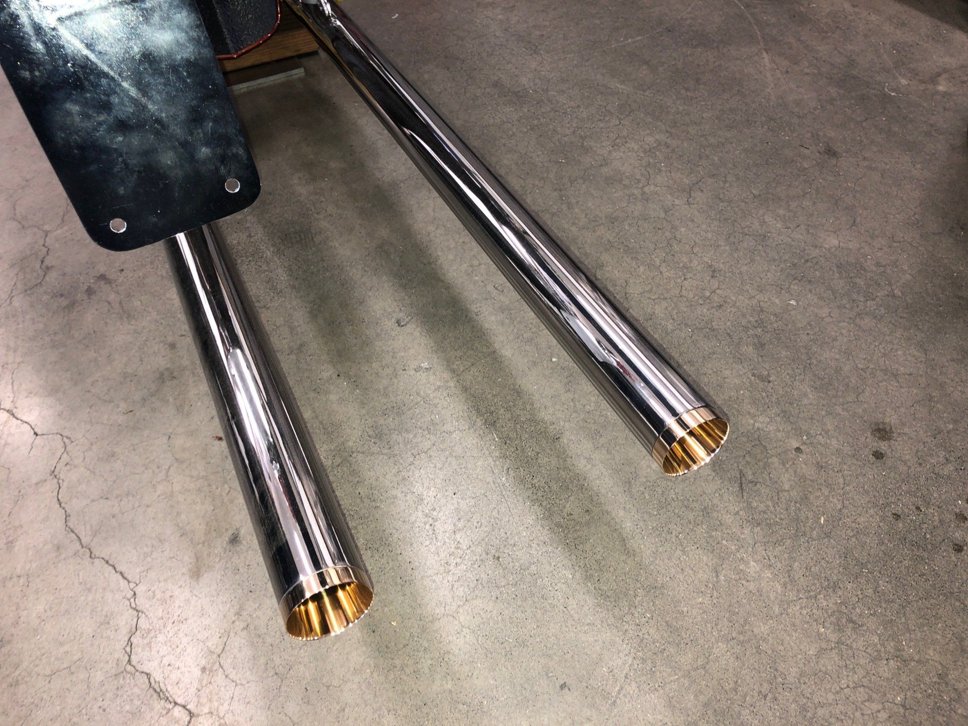 A pair of chrome pipes are sitting on a concrete floor.