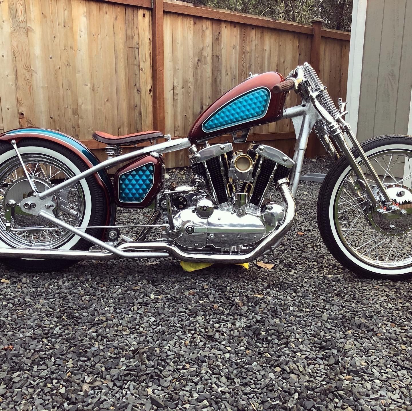 A motorcycle is parked on gravel in front of a wooden fence.