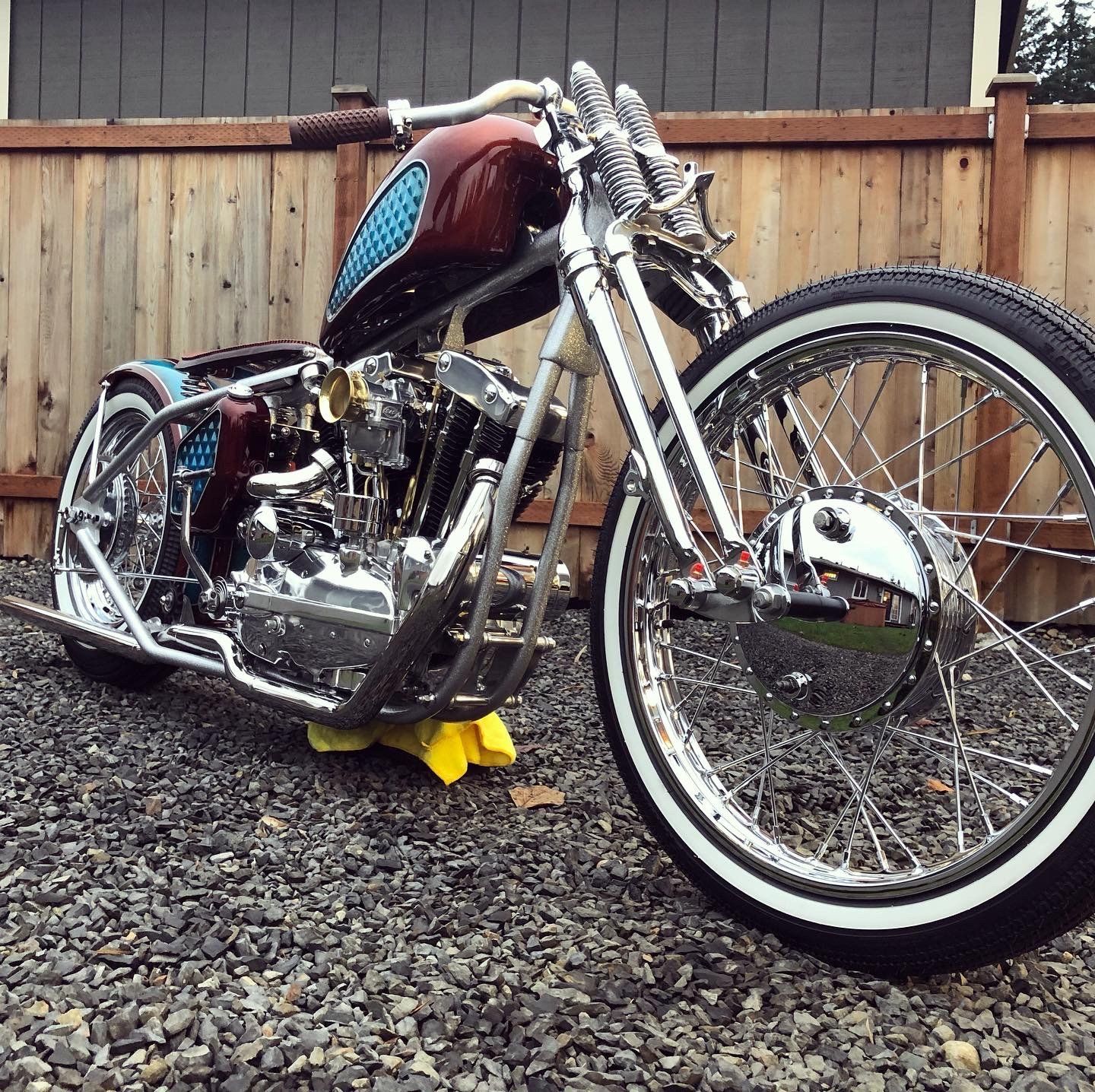 A motorcycle is parked on gravel in front of a wooden fence