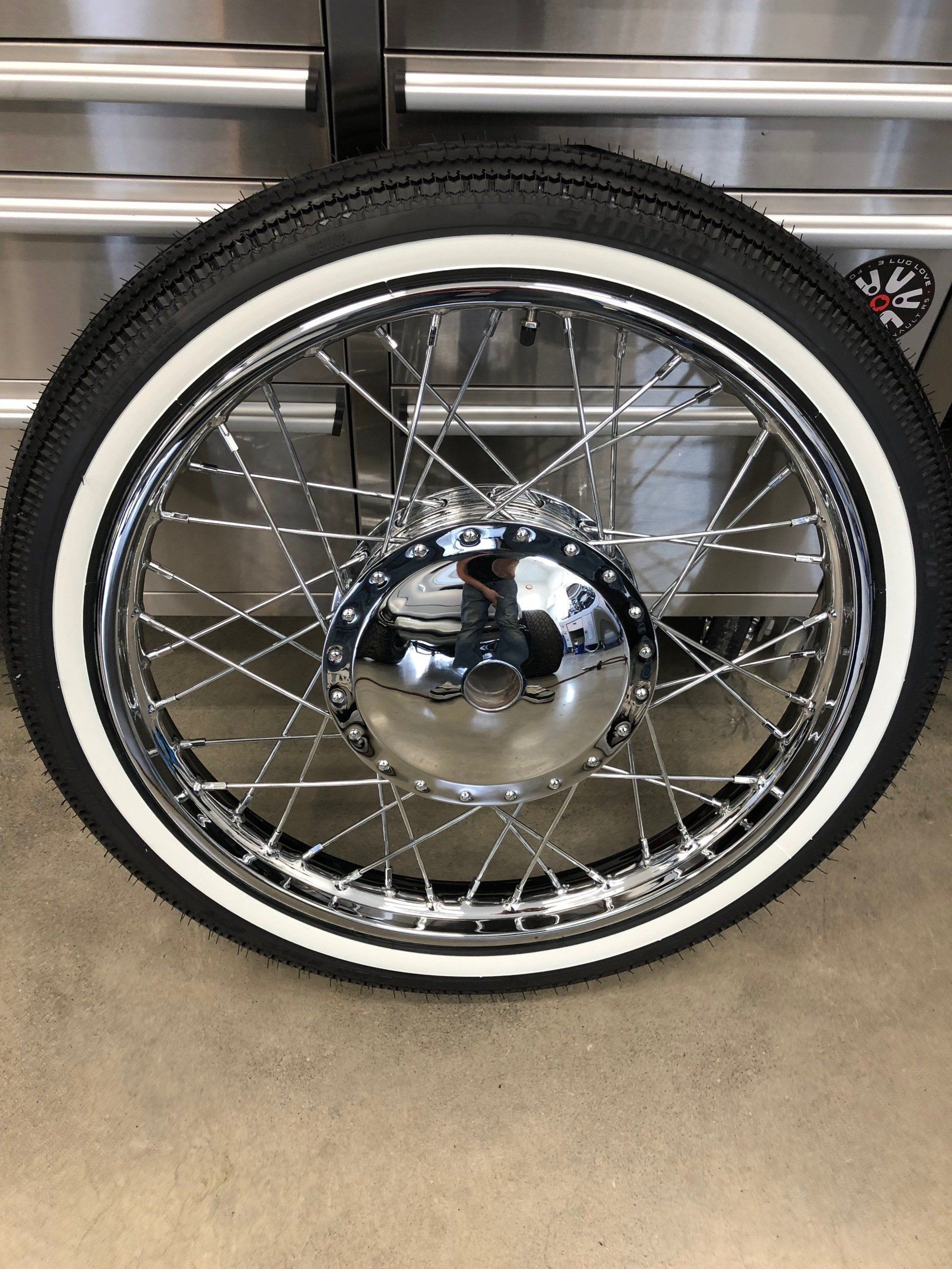 A close up of a motorcycle wheel with a white tire.