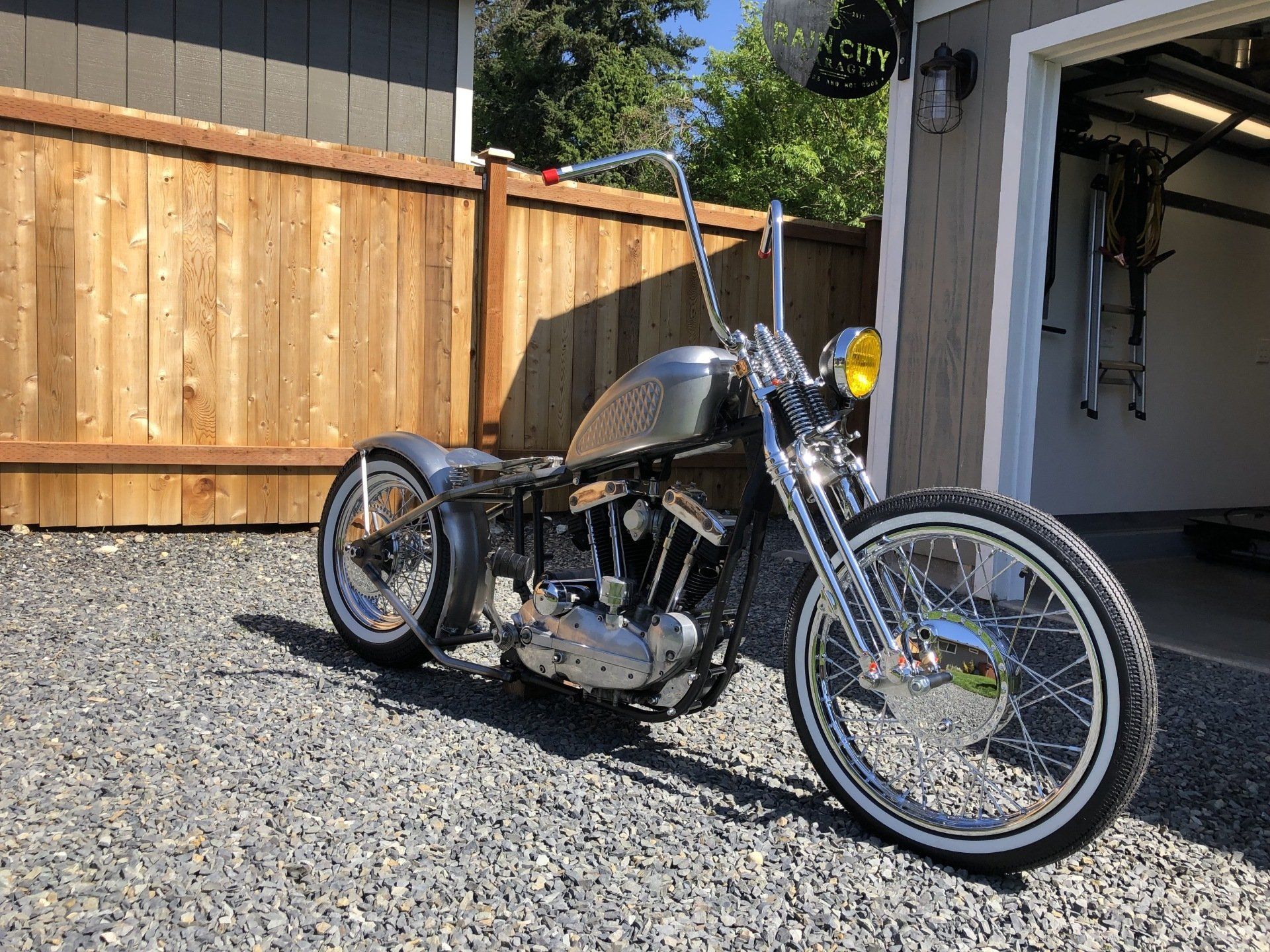 A motorcycle is parked in front of a garage next to a wooden fence.
