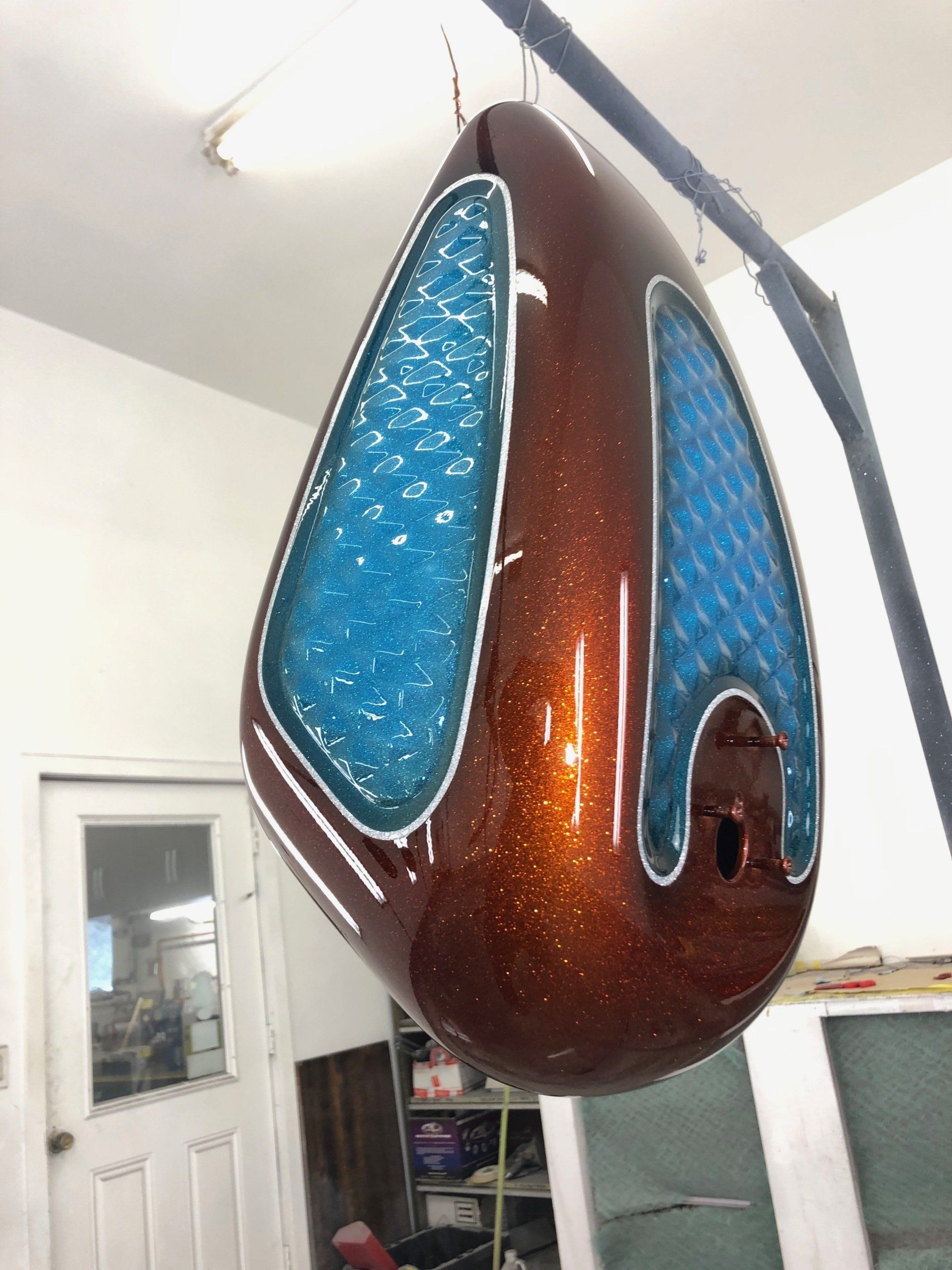 A brown and blue motorcycle tank is hanging from the ceiling