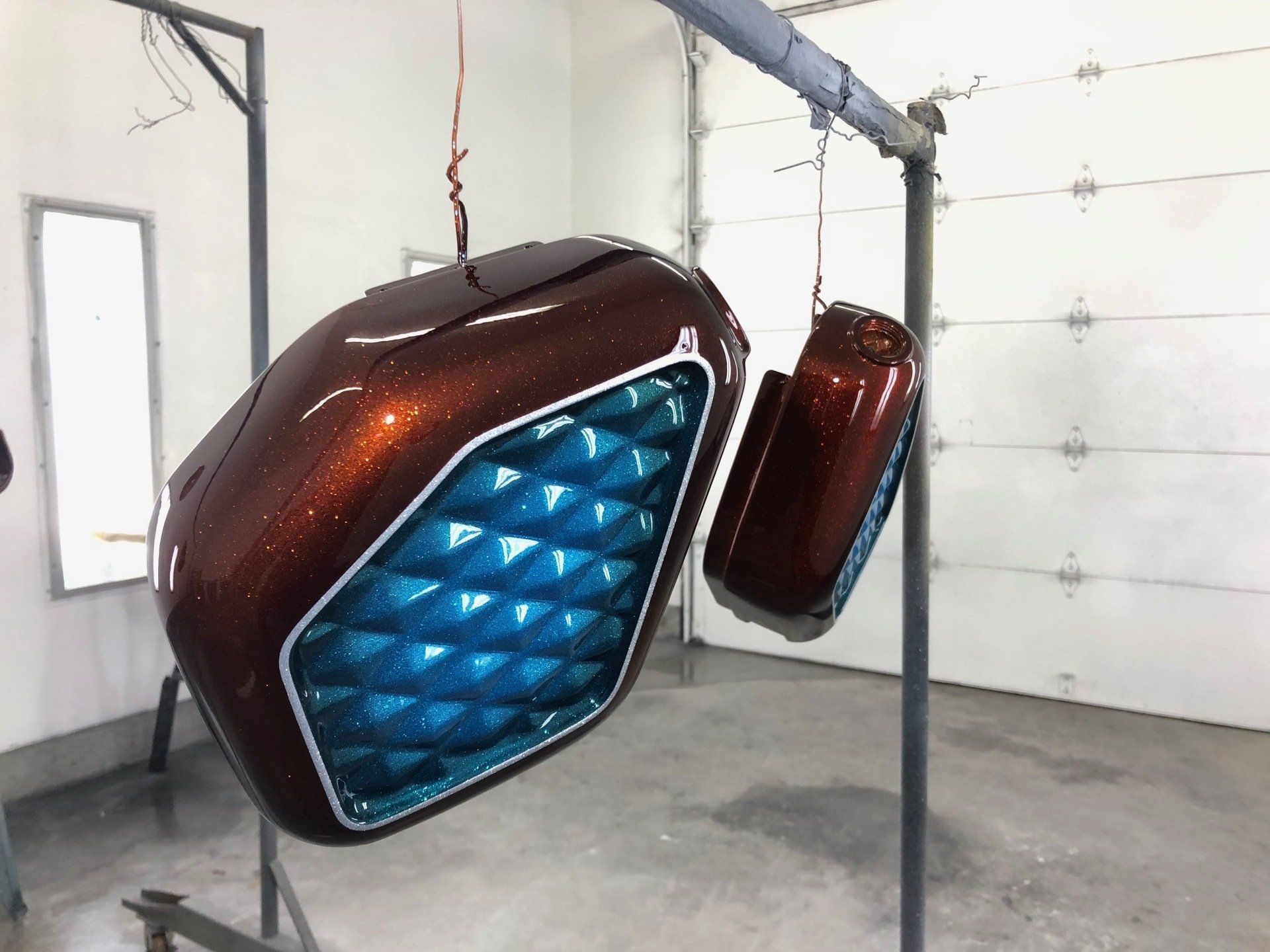 Two motorcycle tanks are hanging from a rack in a garage.