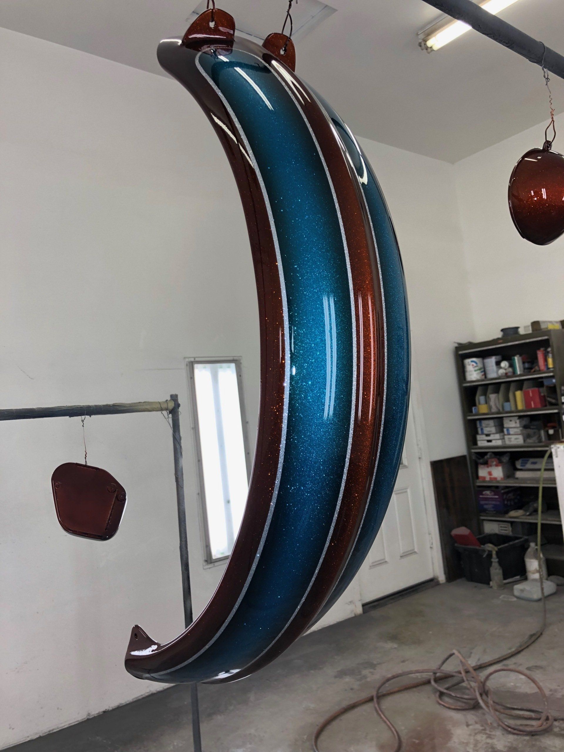 A crescent moon shaped object is being painted in a garage