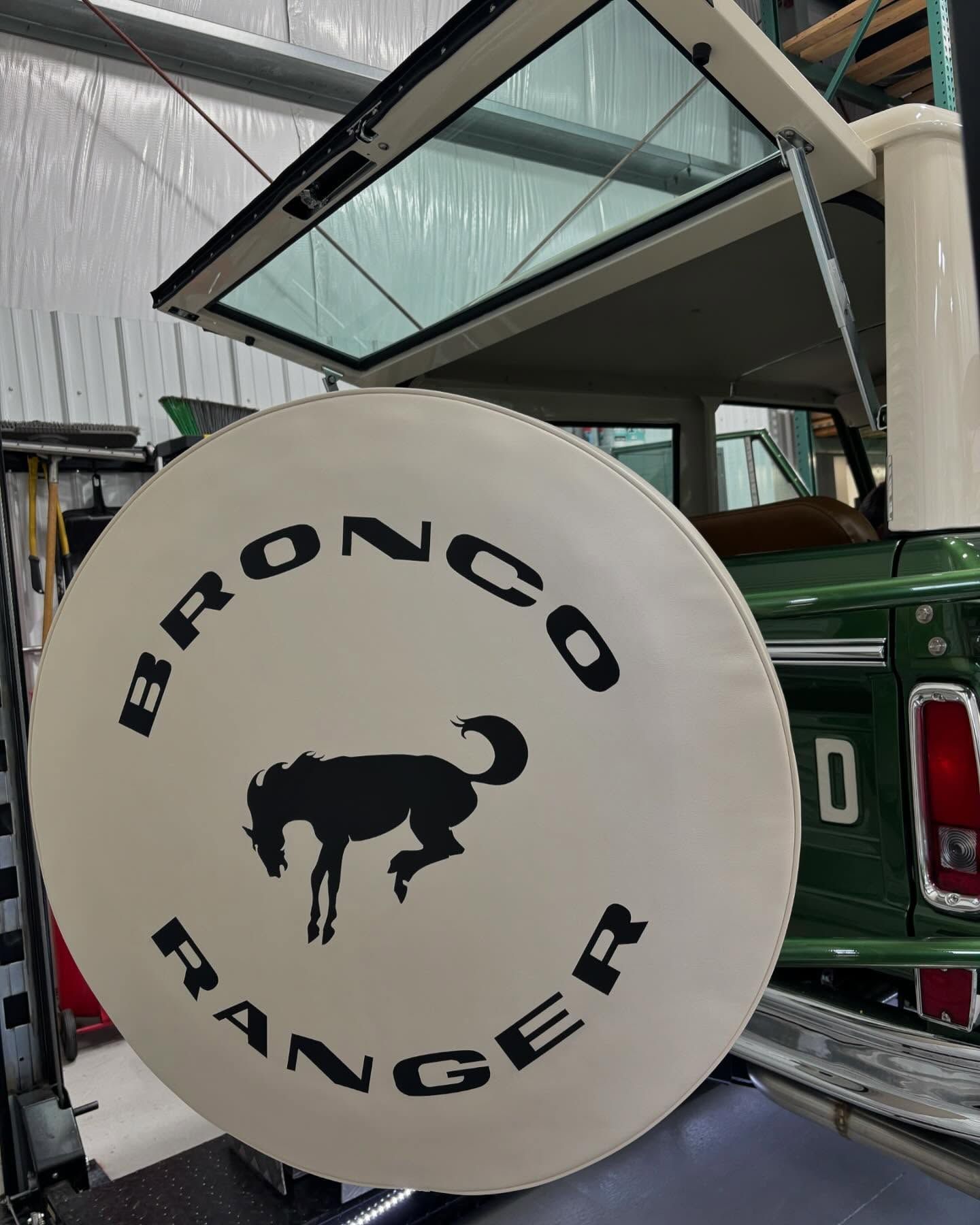 A bronco ranger tire cover is sitting on the back of a green truck.